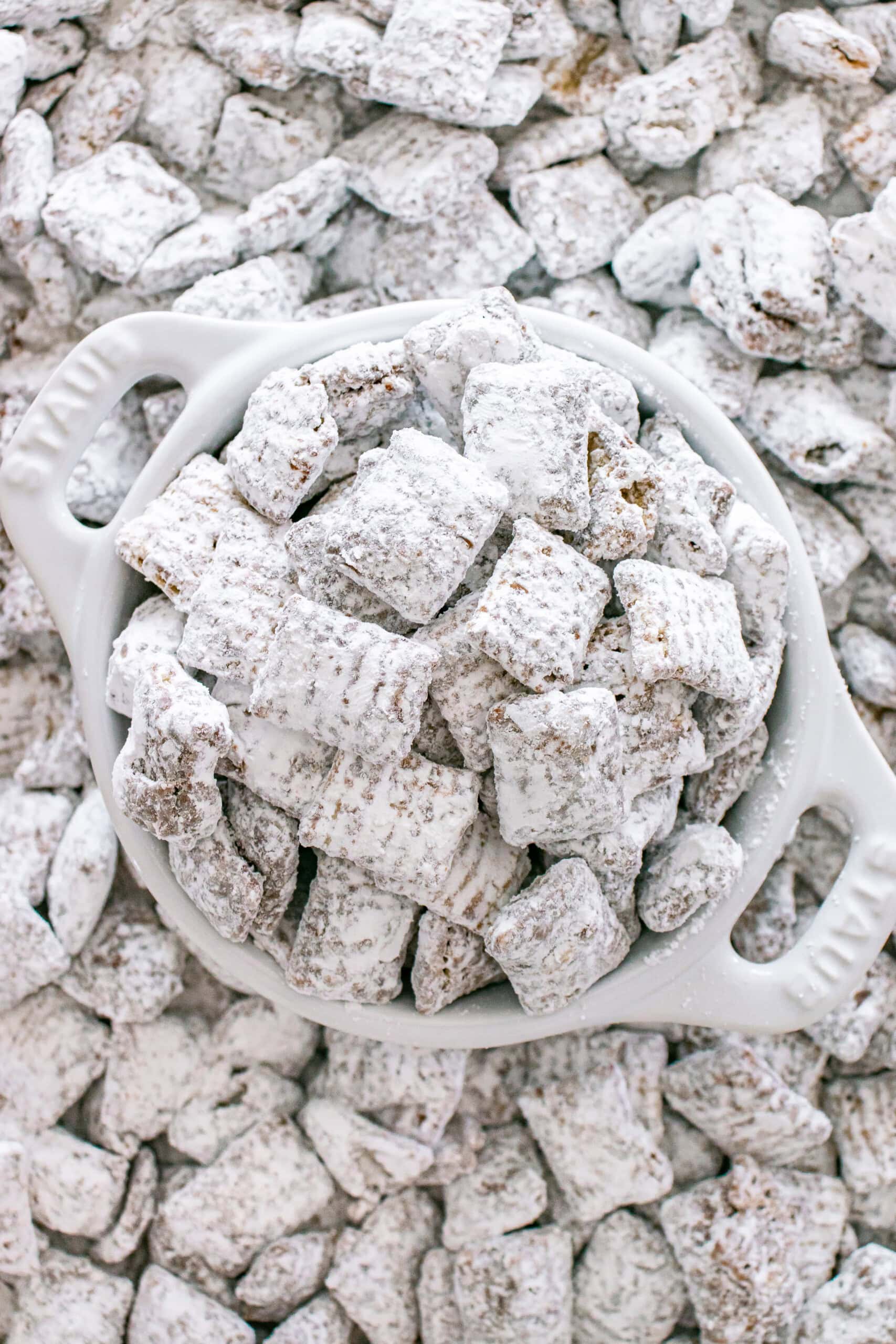Muddy Buddies coated in powdered sugar piled in a white serving bowl.