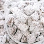 Muddy Buddies coated in powdered sugar piled in a white serving bowl.
