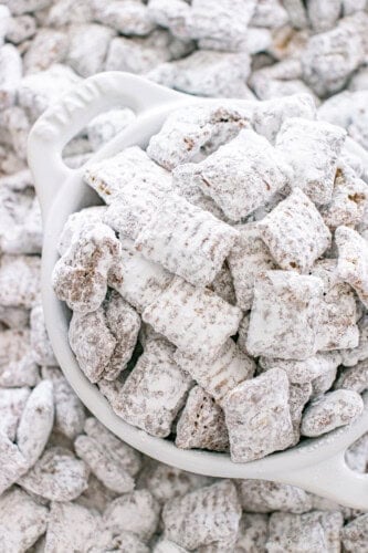 Muddy Buddies coated in powdered sugar piled in a white serving bowl.