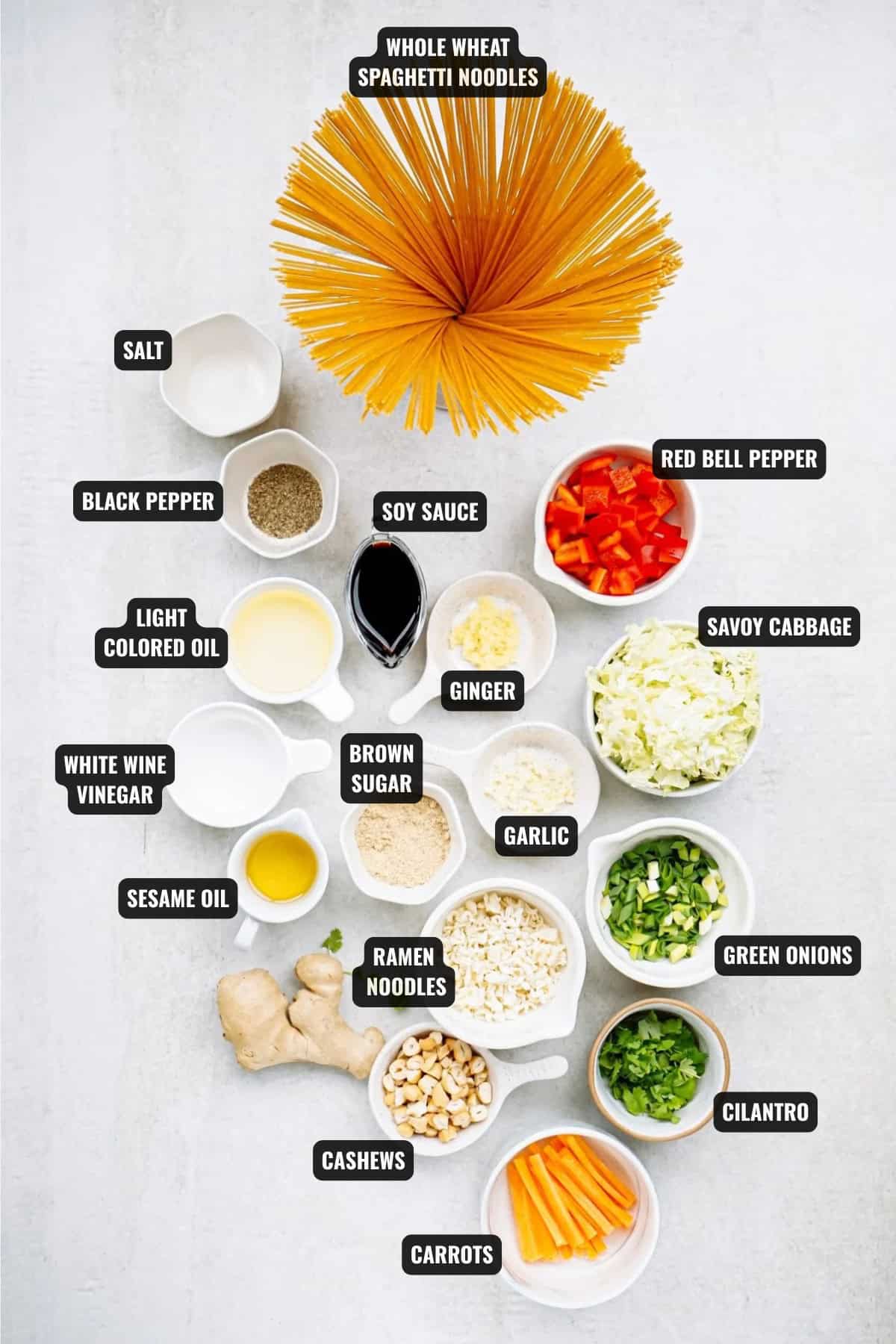 ingredients for sesame noodle salad recipe including spaghetti noodles, red bell pepper, savoy cabbage, green onions, cilantro, carrots, cashews, ramen noodles, garlic, ginger, brown sugar, soy sauce, sesame oil, light-colored oil, white wine vinegar, black pepper and salt