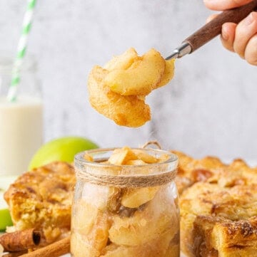 Homemade Apple Pie Filling with tender cinnamon-coated apples in a glass jar and a spoonful lifted above.