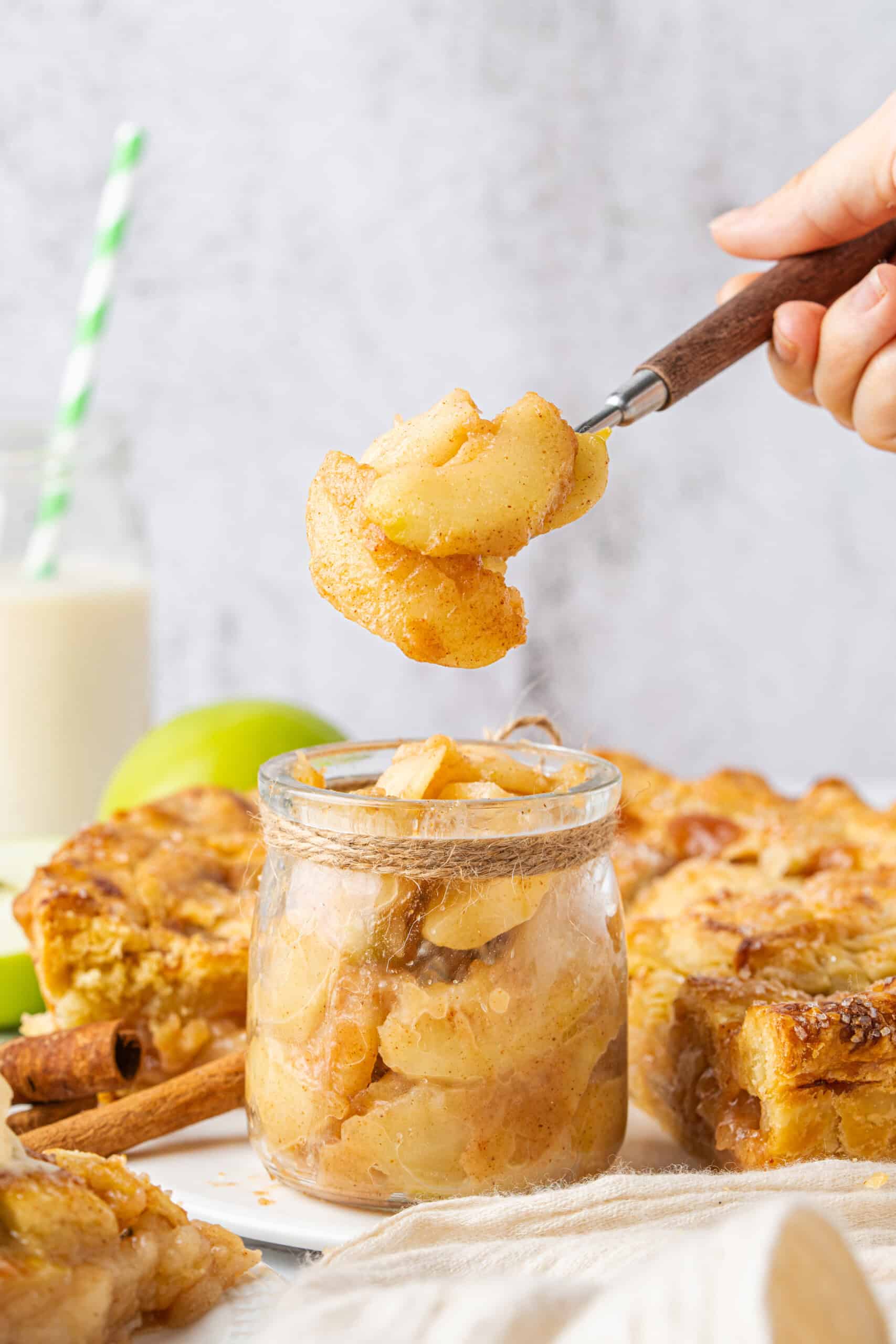 Homemade Apple Pie Filling with tender cinnamon-coated apples in a glass jar and a spoonful lifted above.