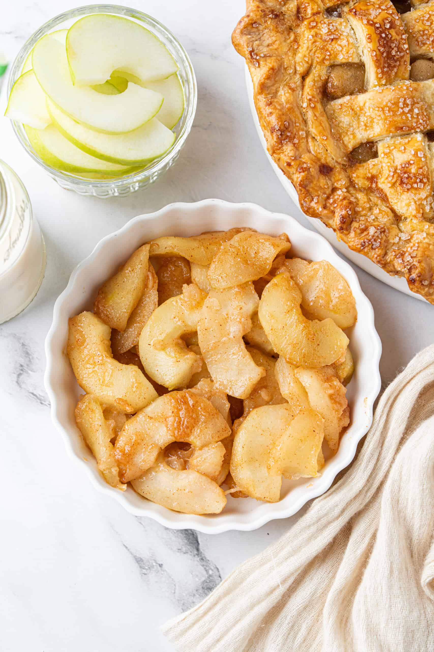 Apple Pie Filling with tender cinnamon-spiced slices in a white bowl beside a golden lattice pie.