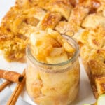 Homemade Apple Pie Filling with tender cinnamon-coated apple slices in a glass jar, surrounded by golden apple pie and fresh apples.