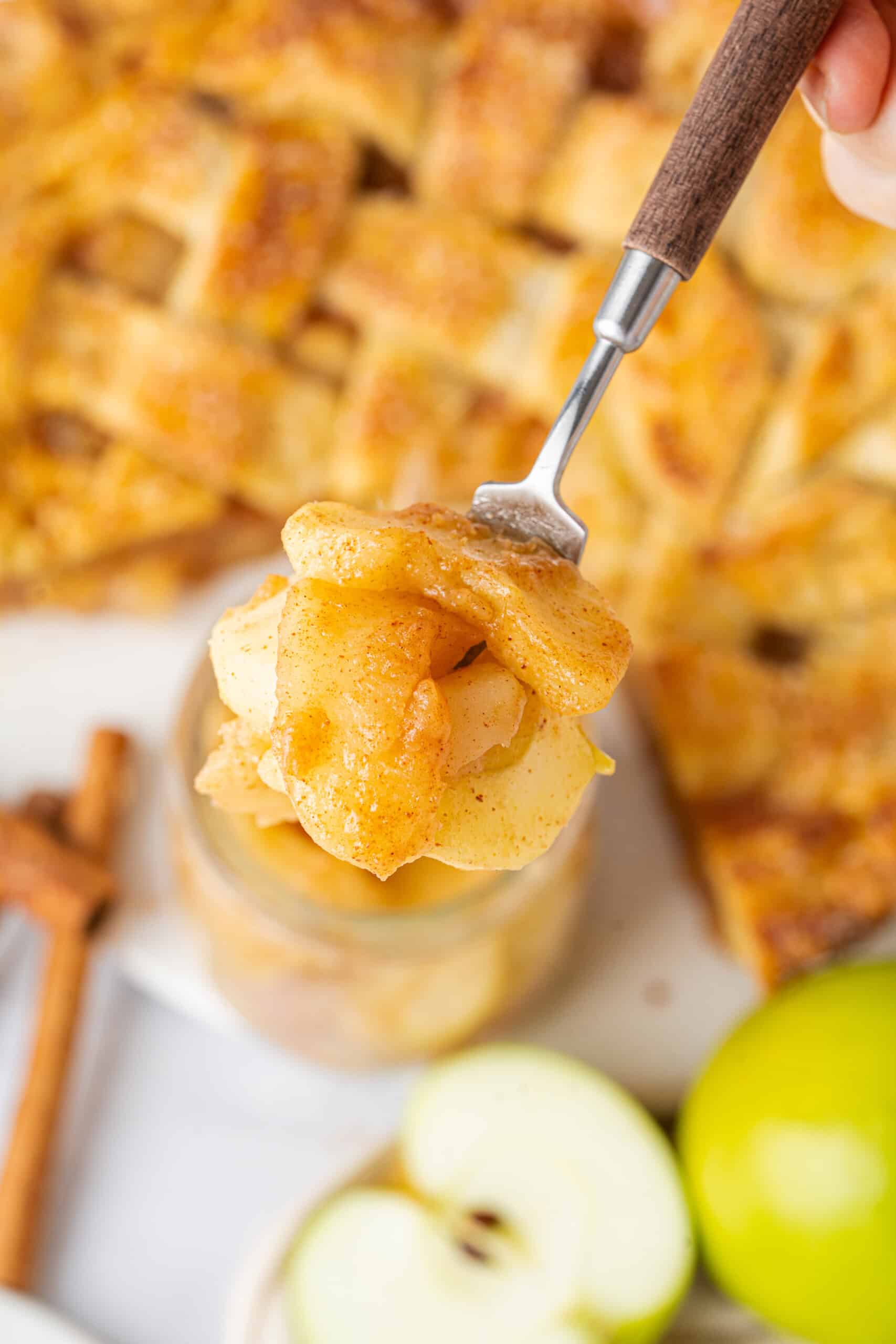 cinnamon-spiced apple slices on a fork, with a golden lattice pie in the background.