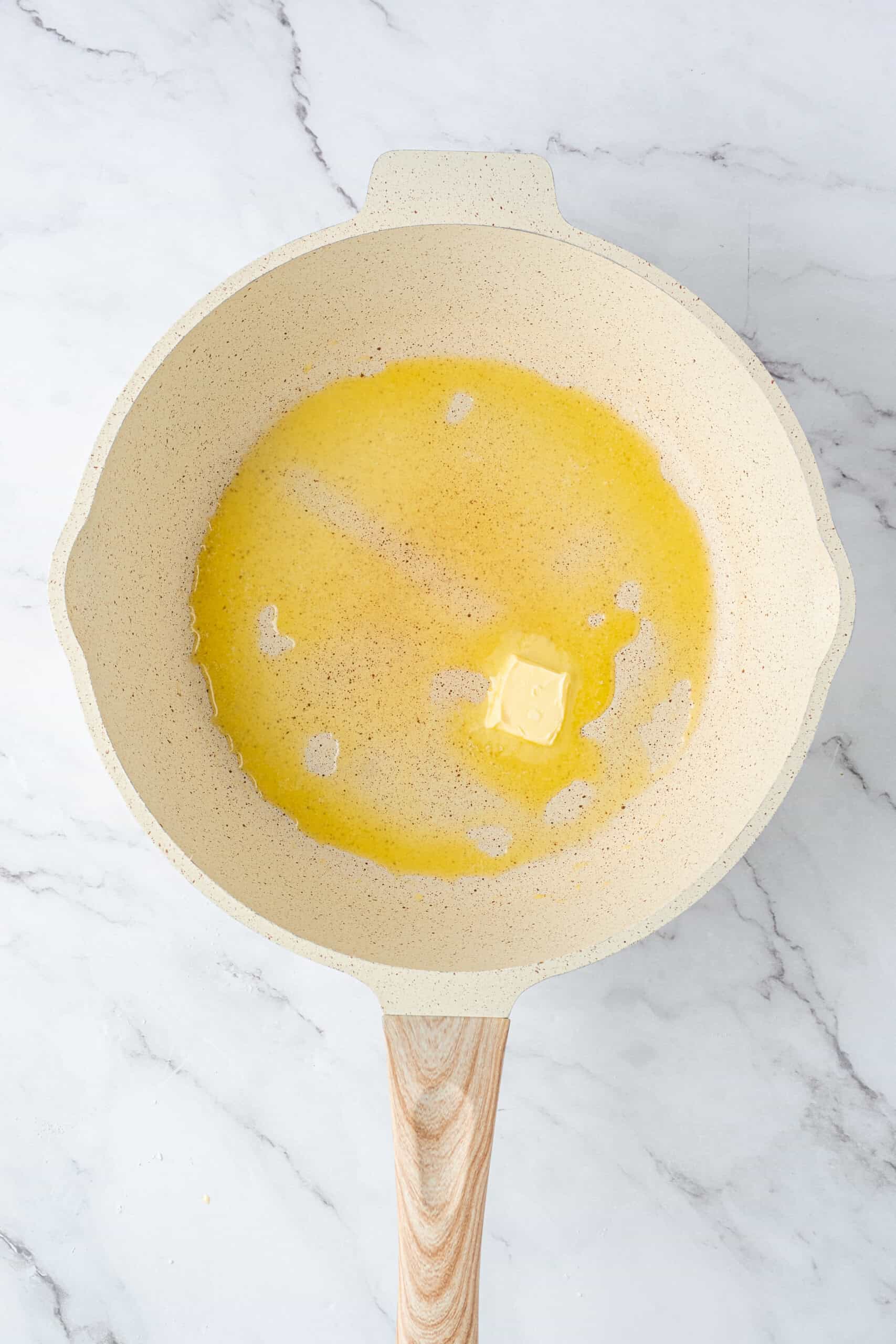 Butter melting in a cream-colored skillet with a wooden handle