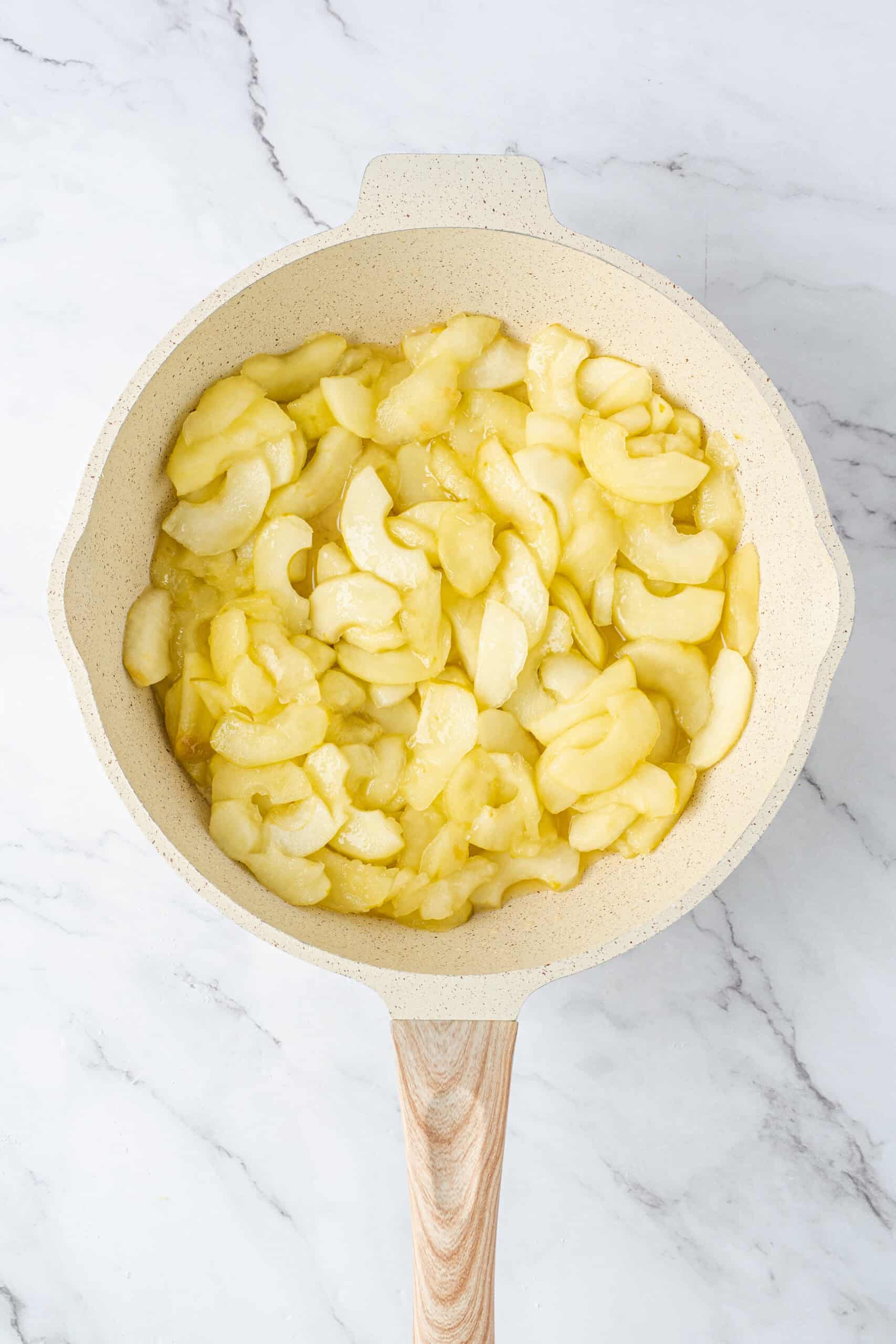 Softened apple slices coated in a glossy butter and sugar mixture in a cream-colored skillet.