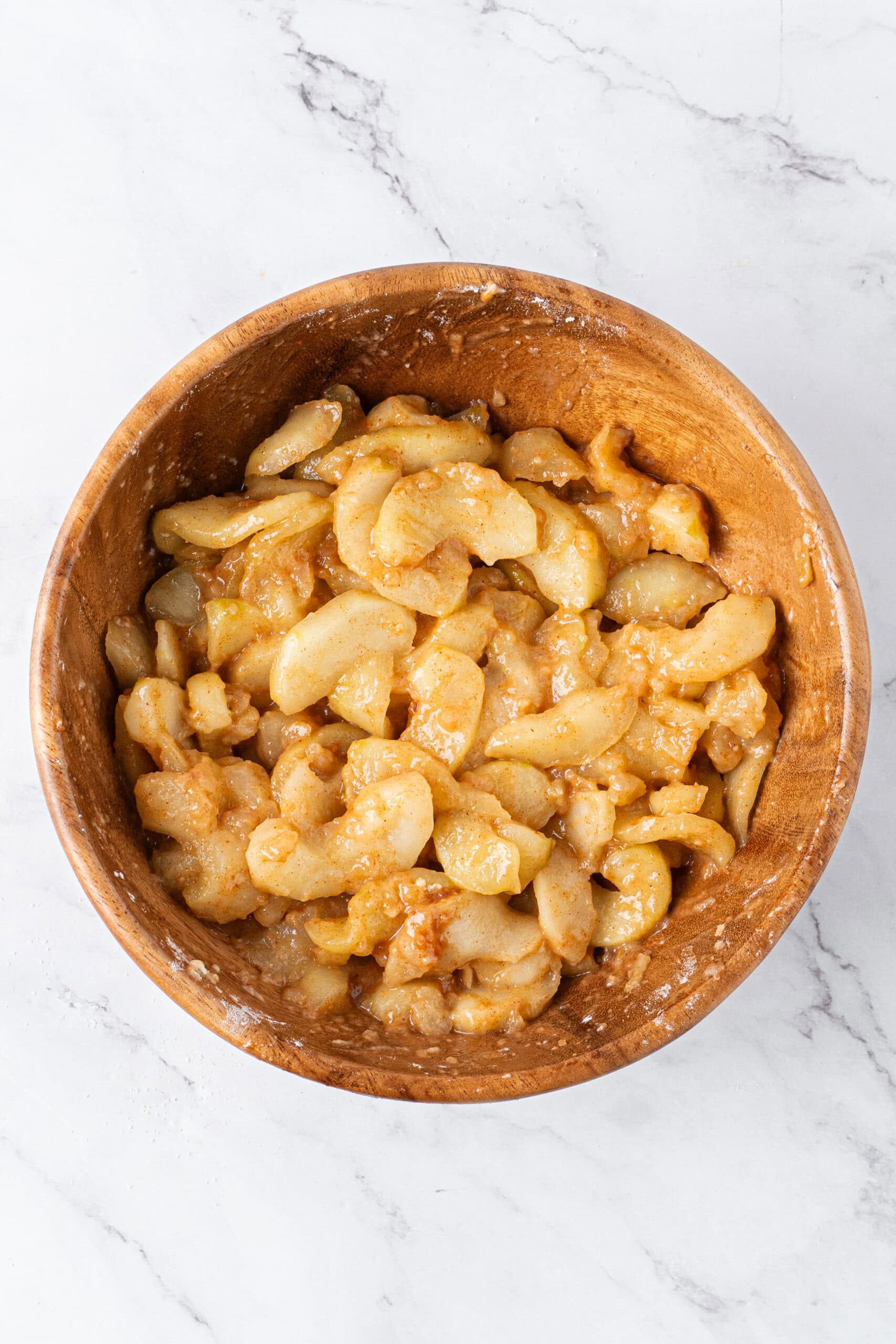 Cooked apple slices mixed with cinnamon, sugar, and flour in a wooden bowl, forming a thick apple pie filling.