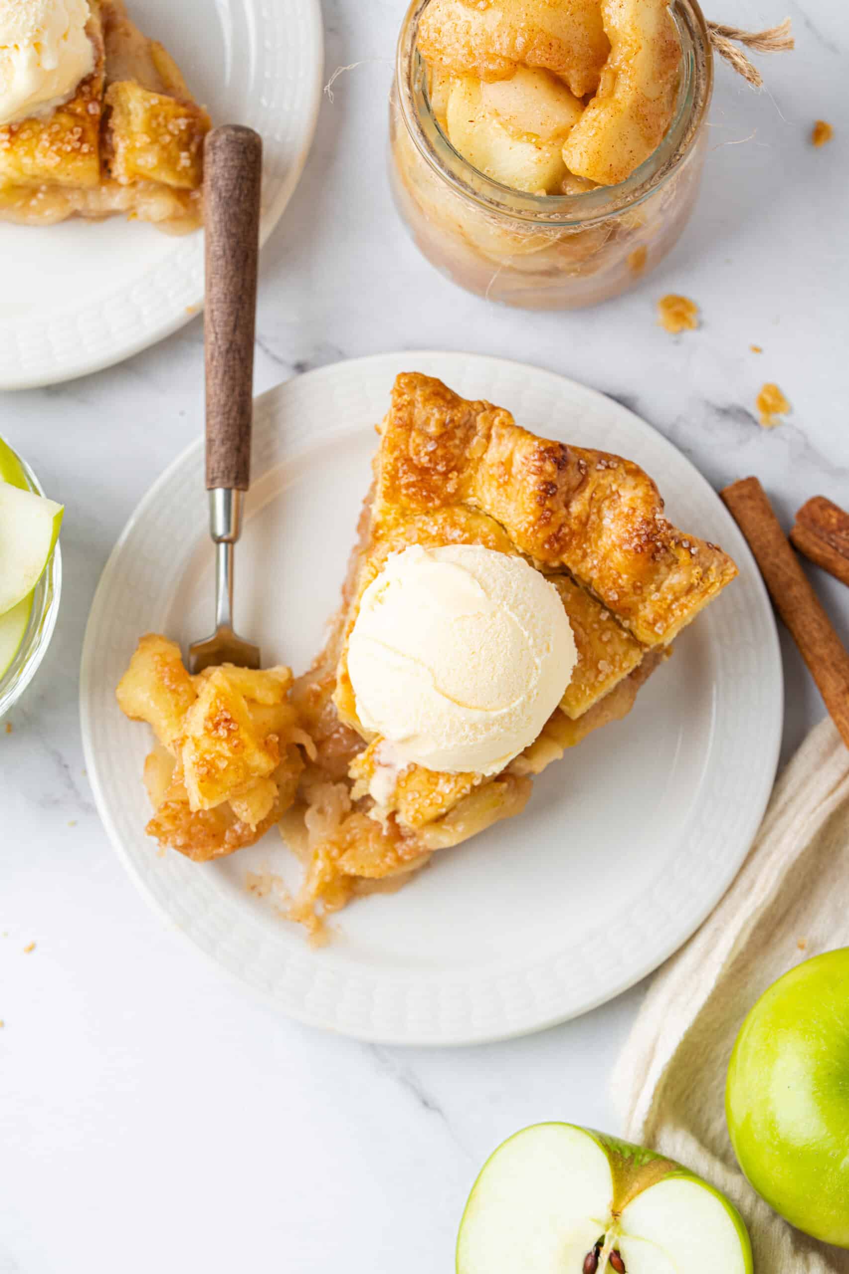 Overhead view of a slice from a homemade apple pie with a golden, flaky lattice crust, tender cinnamon-spiced apple filling, and a scoop of vanilla ice cream on top.