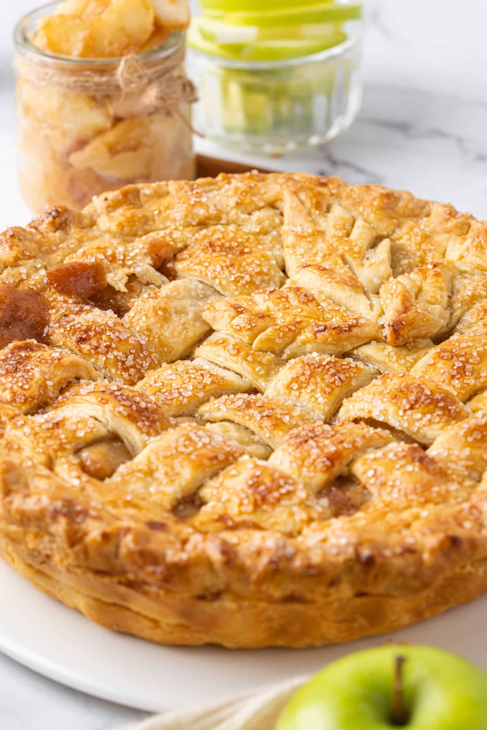 Close-up of a homemade apple pie with a golden, flaky lattice crust sprinkled with coarse sugar and filled with tender, cinnamon-spiced apples.