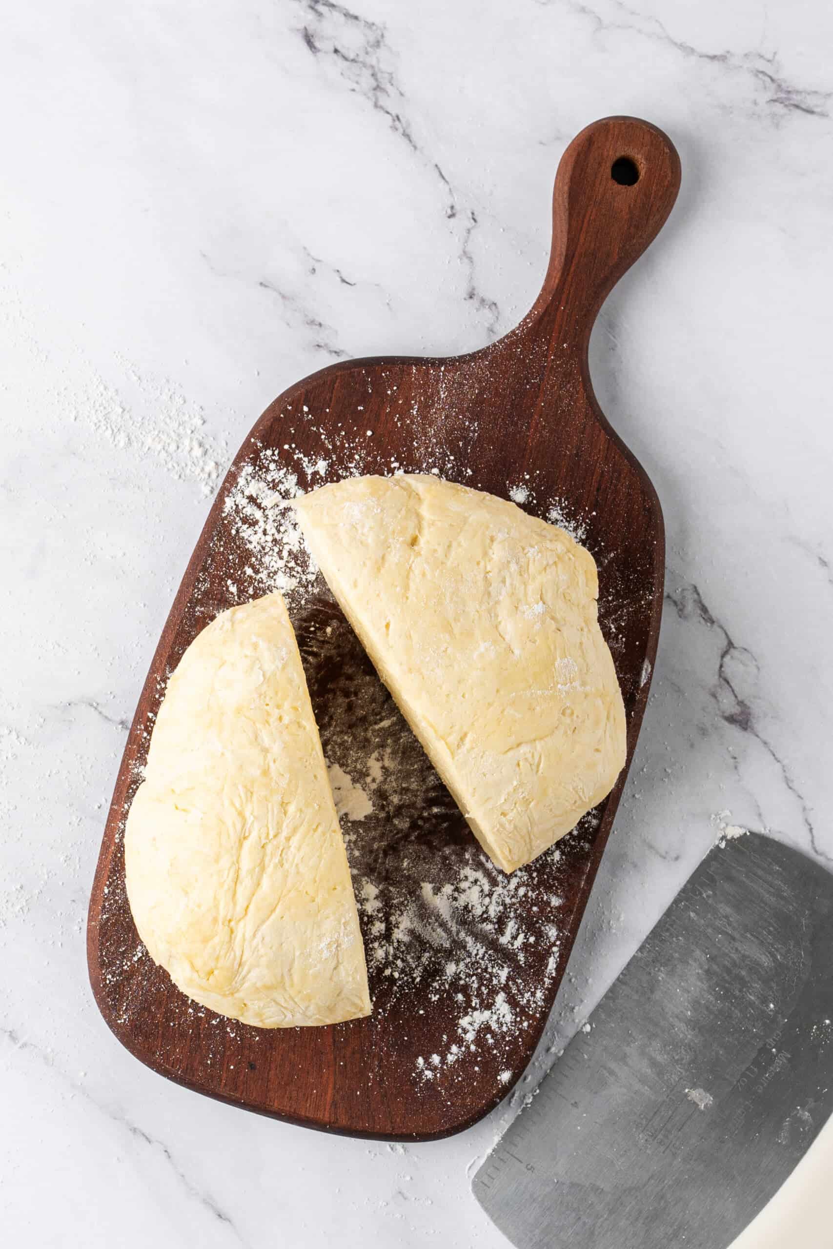 pie crust dough divided into two portions on a floured wooden cutting board.