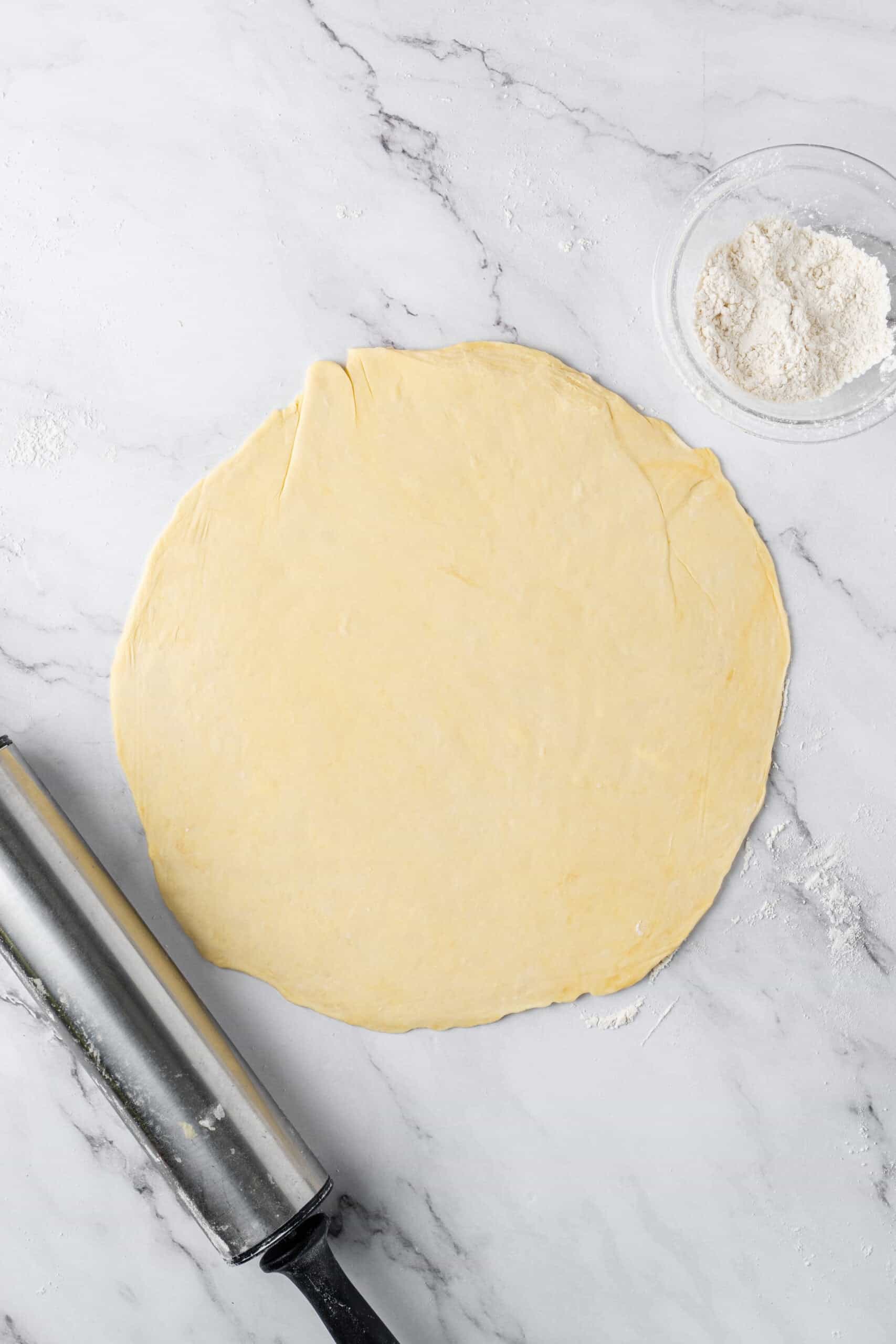 pie crust dough rolled into a large circle on a lightly floured marble surface.