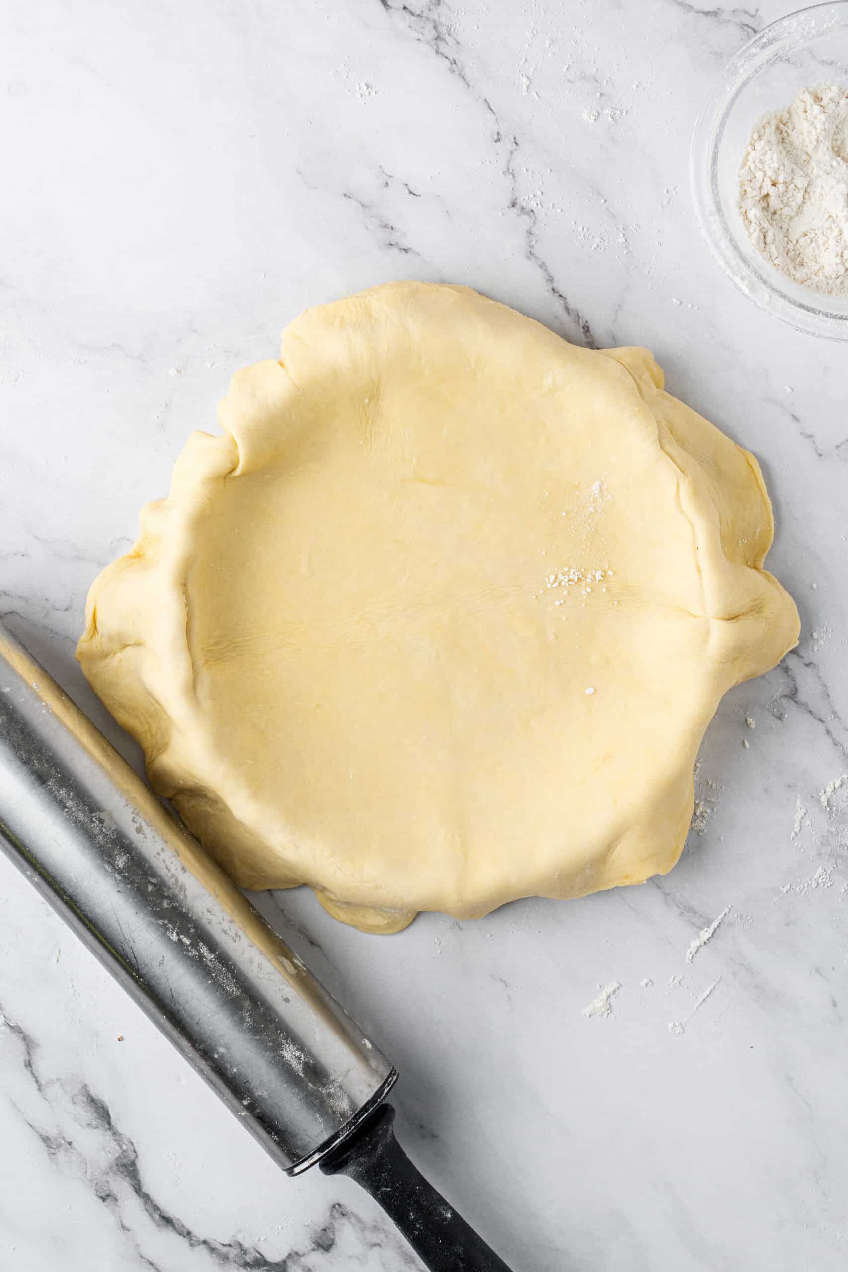 Rolled-out pie crust dough draped over a pie dish with excess dough hanging over the edges.