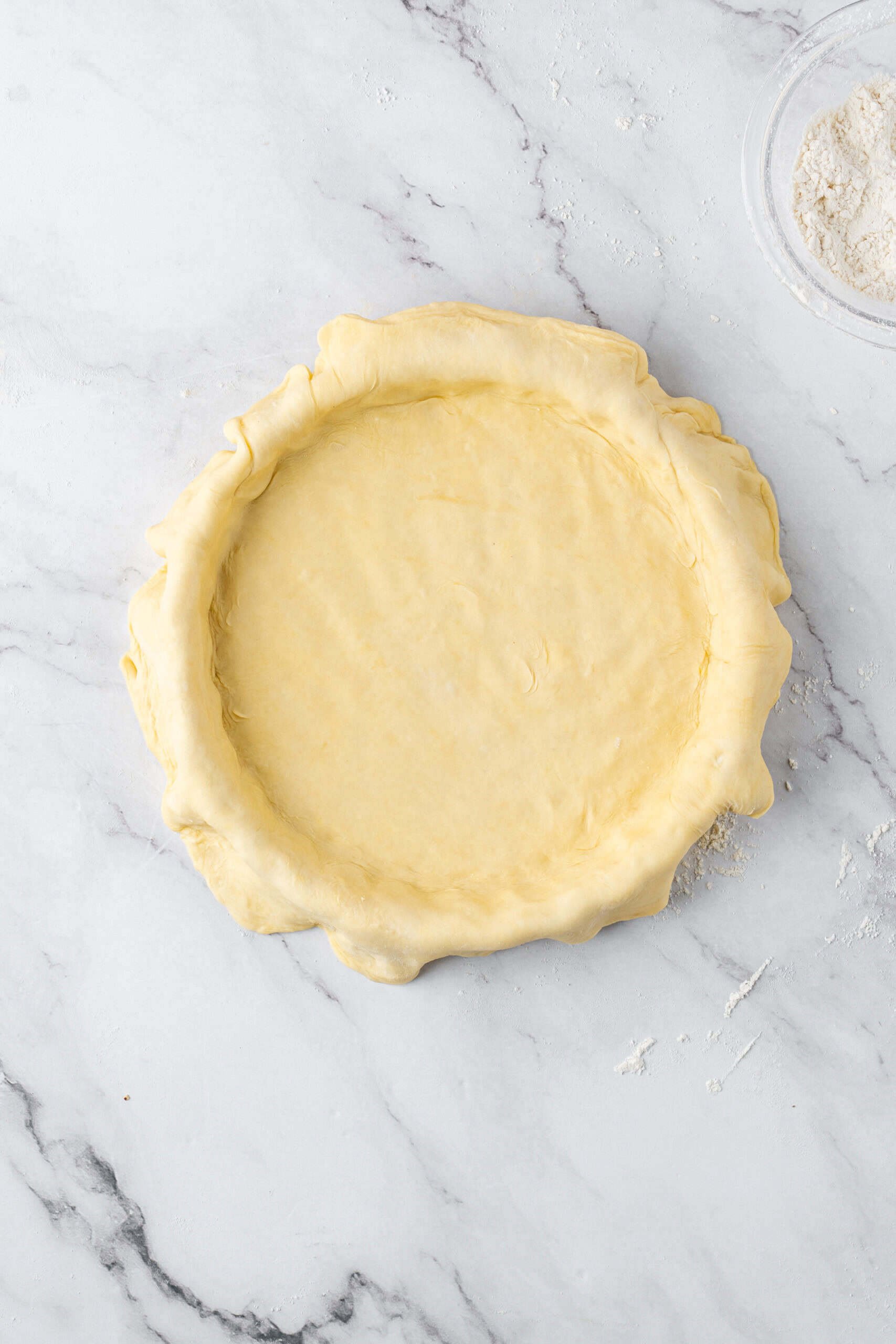Homemade pie crust dough pressed into a pie dish with the excess dough folded around the edges.