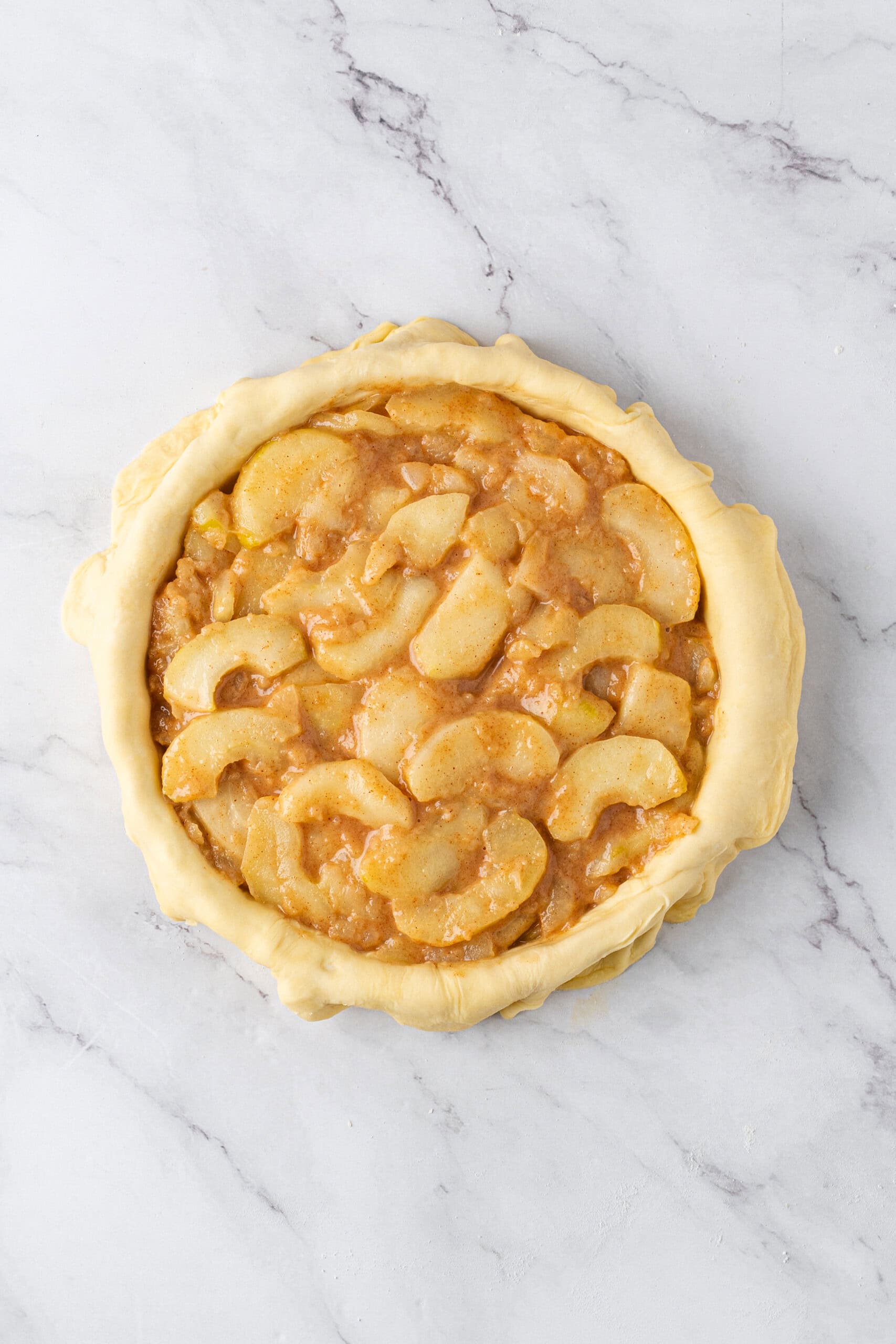 pie crust filled with sliced apples coated in a cinnamon-spiced filling, ready for the top crust.
