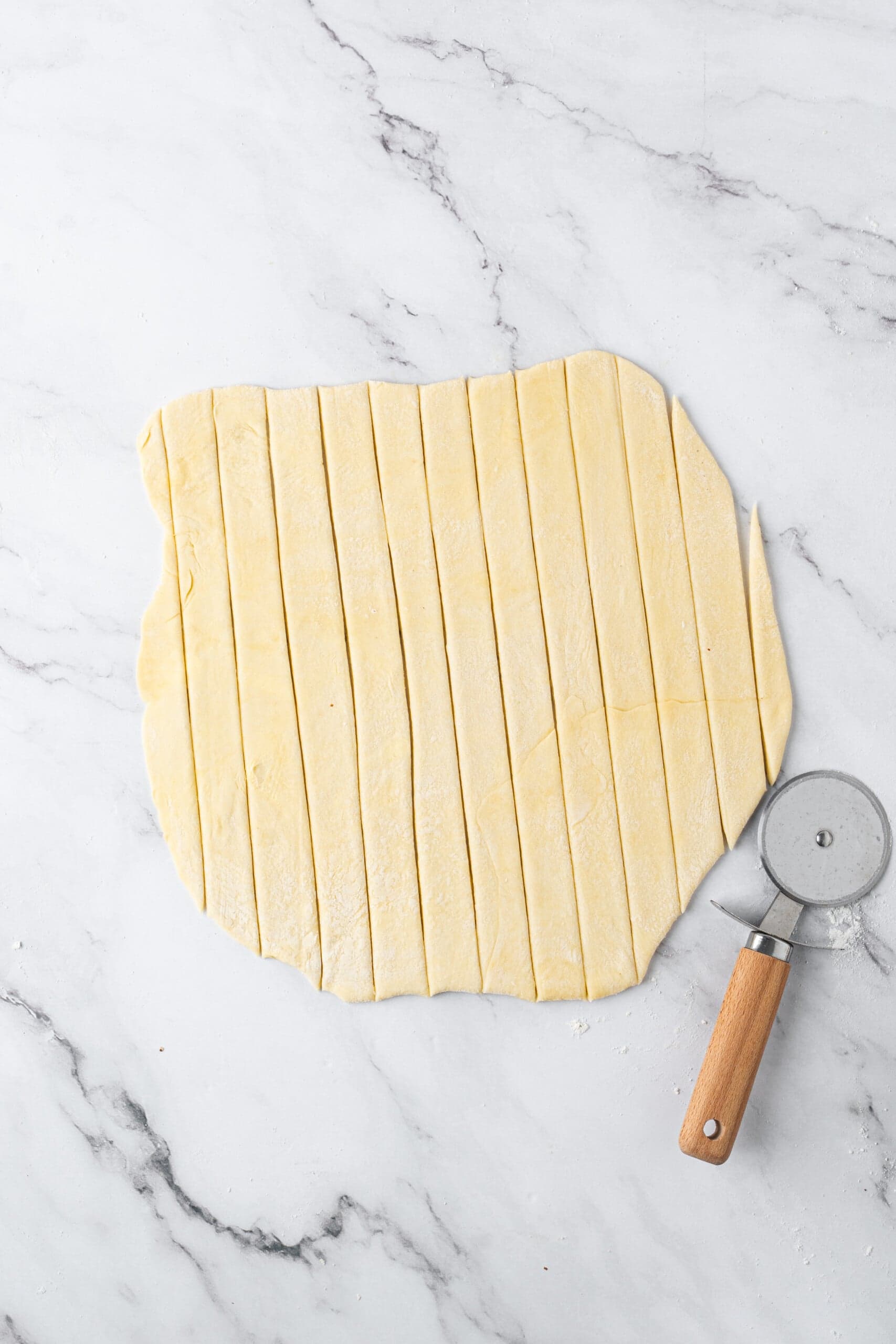 Rolled-out pie crust cut into even strips with a pastry cutter for a lattice apple pie topping.