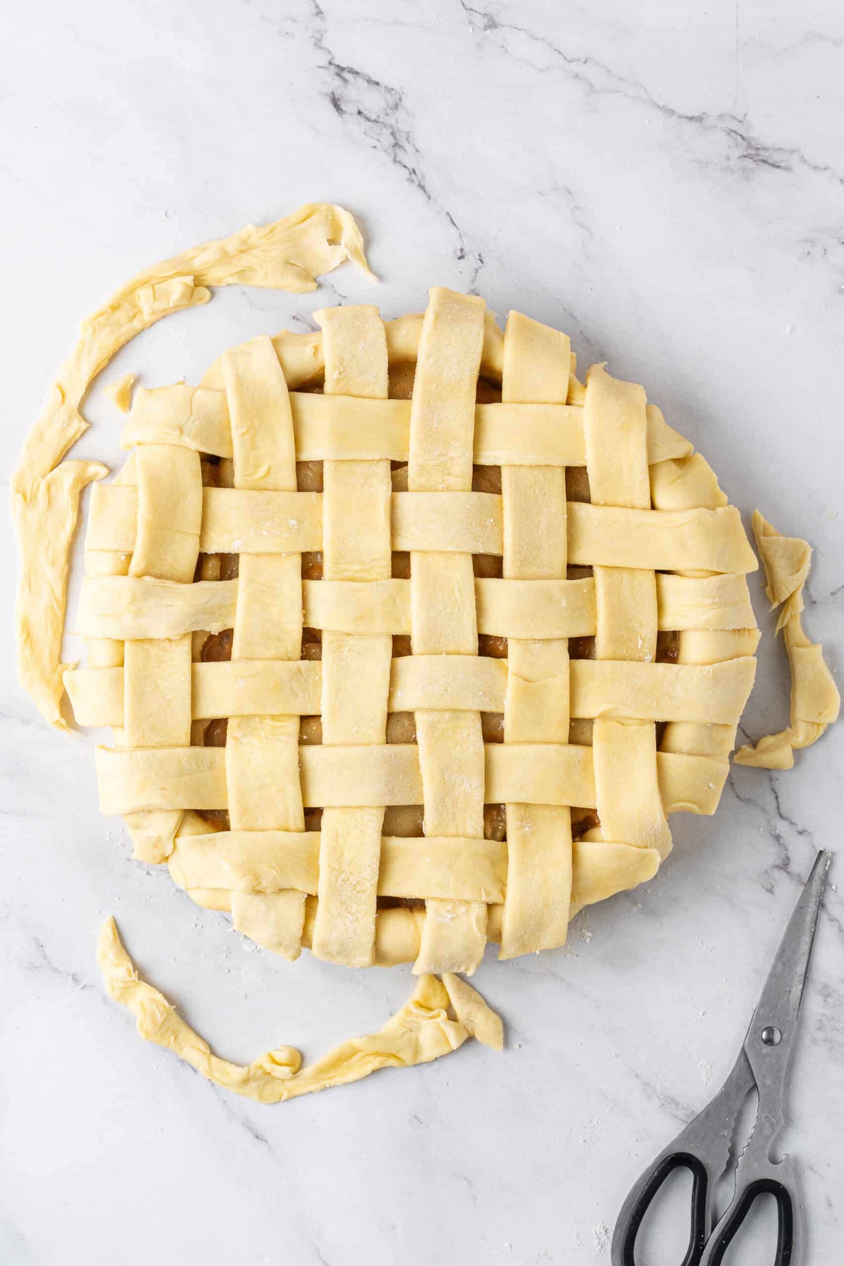 Unbaked pie with a woven lattice crust and trimmed dough scraps surrounding the pie.