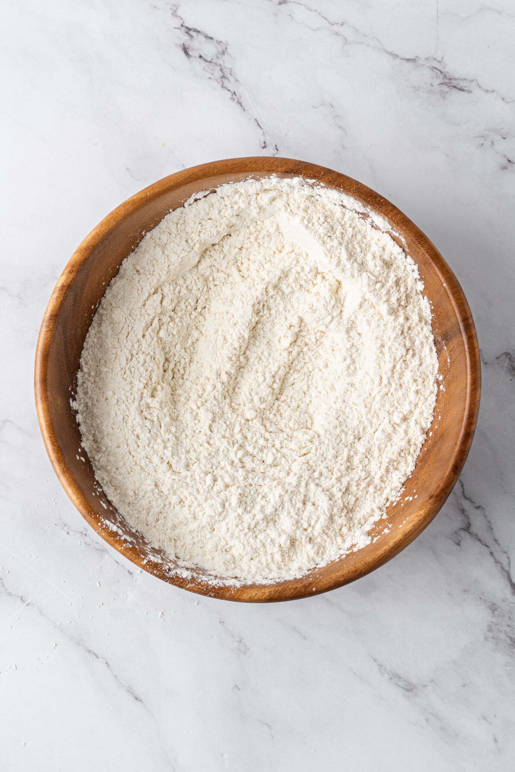 A wooden bowl filled with mixed dry ingredients on a white marble countertop.