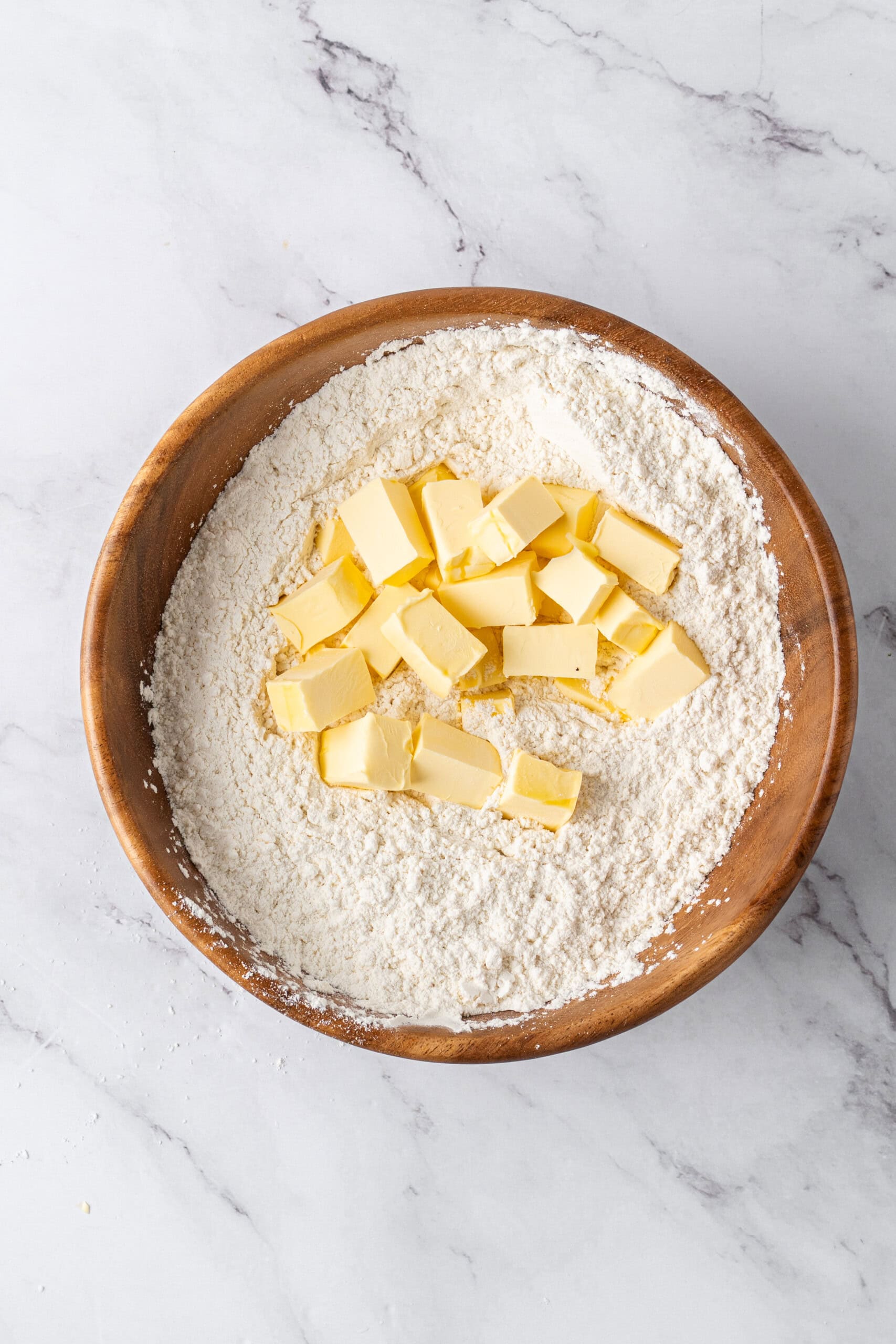 Cubed butter added to a wooden bowl of flour mixture