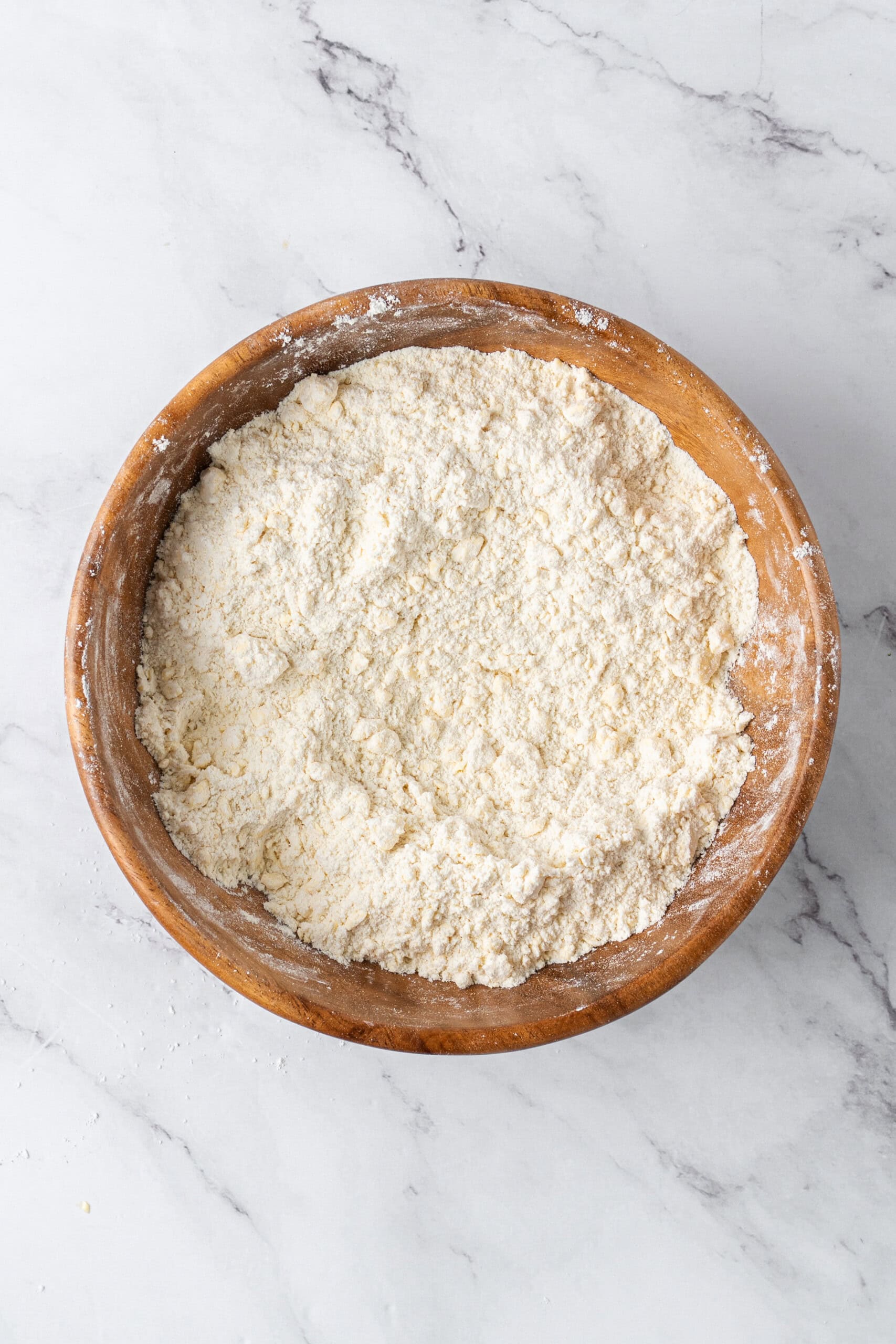 Flour and butter combined into a coarse, crumbly mixture in a wooden bowl.
