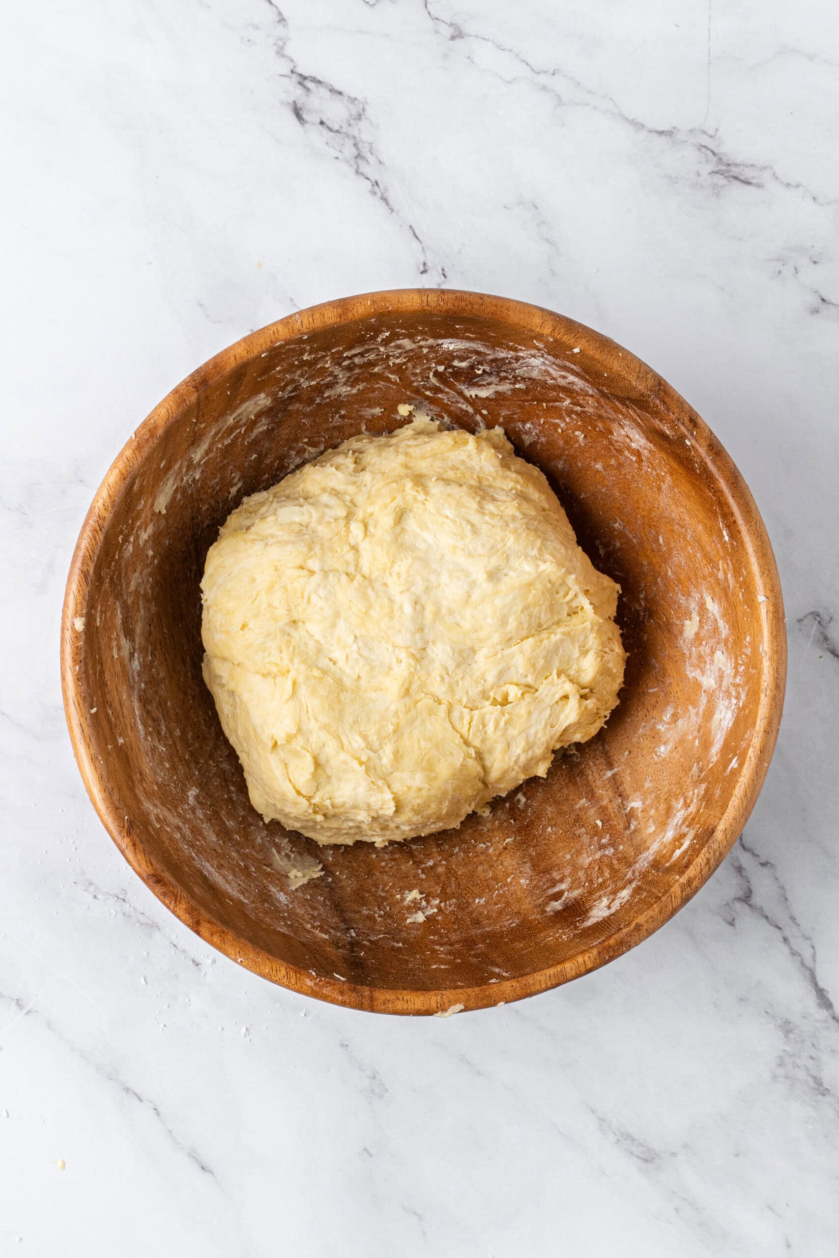 Homemade pie crust dough formed into a rough ball in a wooden mixing bowl.