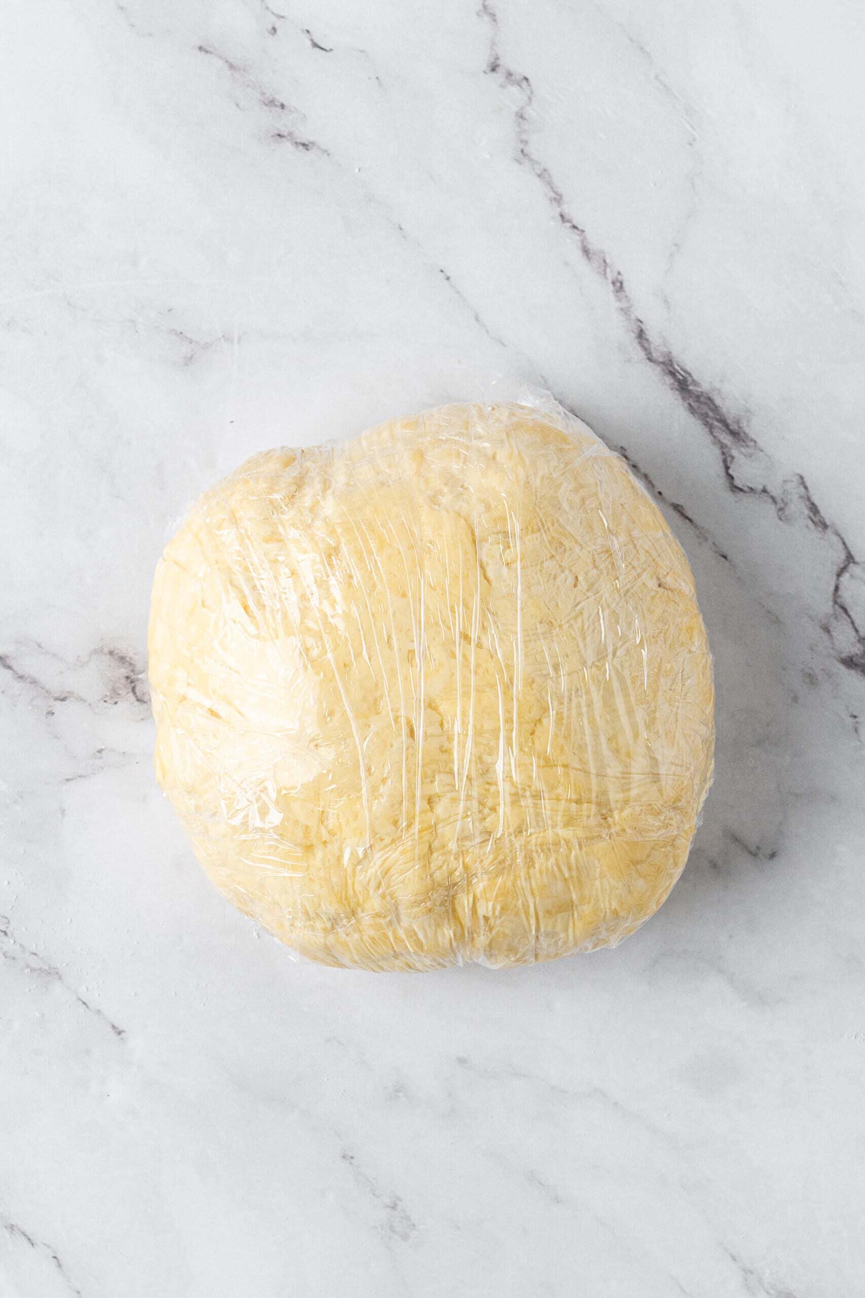 Homemade pie crust dough shaped into a round disc and wrapped tightly in plastic wrap.