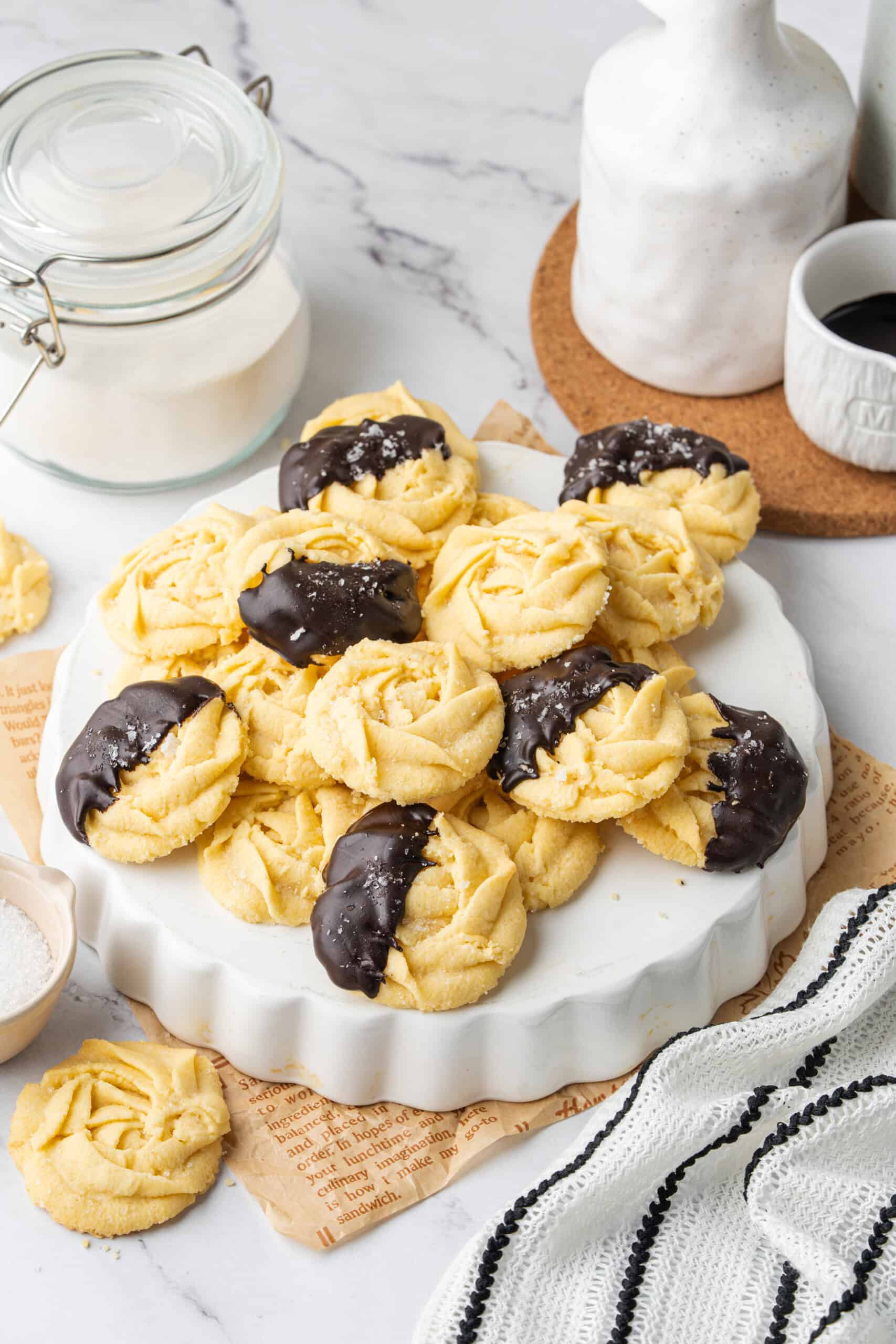 Butter cookies piled on a serving plate, with several dipped in dark chocolate and sprinkled with sugar.