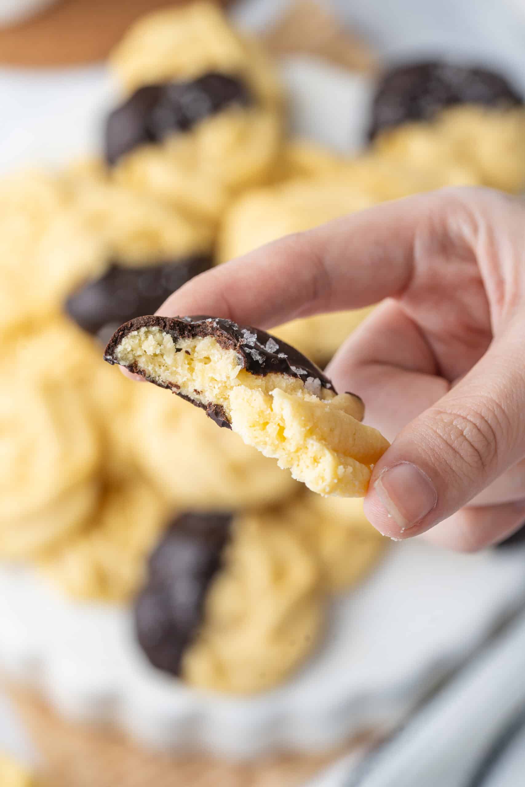 Hand holding a bitten chocolate-dipped butter cookie topped with sugar.