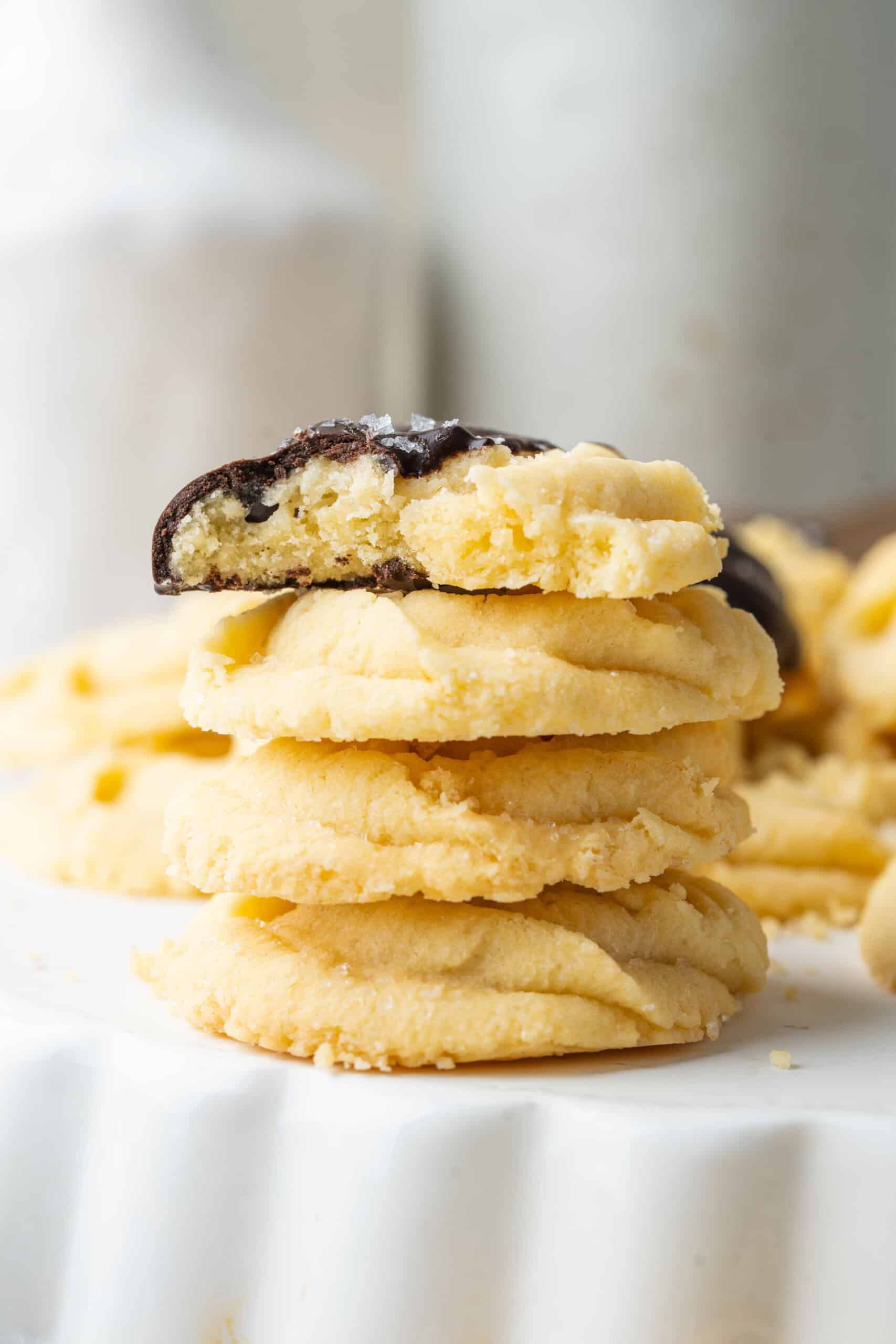 Stack of butter cookies topped with a chocolate-dipped cookie broken in half.