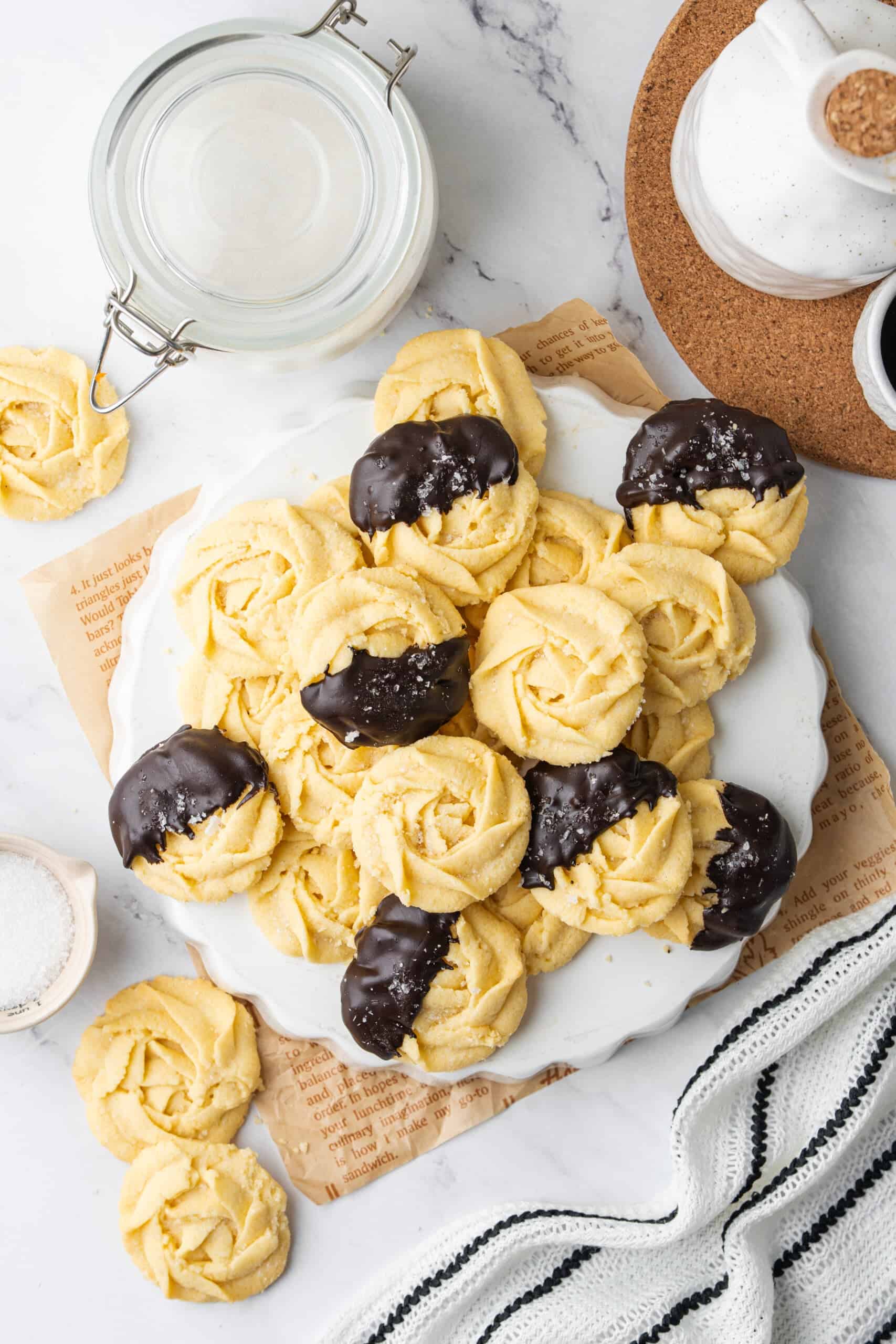Butter cookies on a serving plate, with several dipped in dark chocolate and sprinkled with sugar.