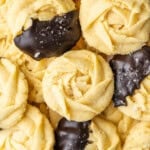 Butter cookies with rosette shapes, some dipped in dark chocolate and sprinkled with sugar.