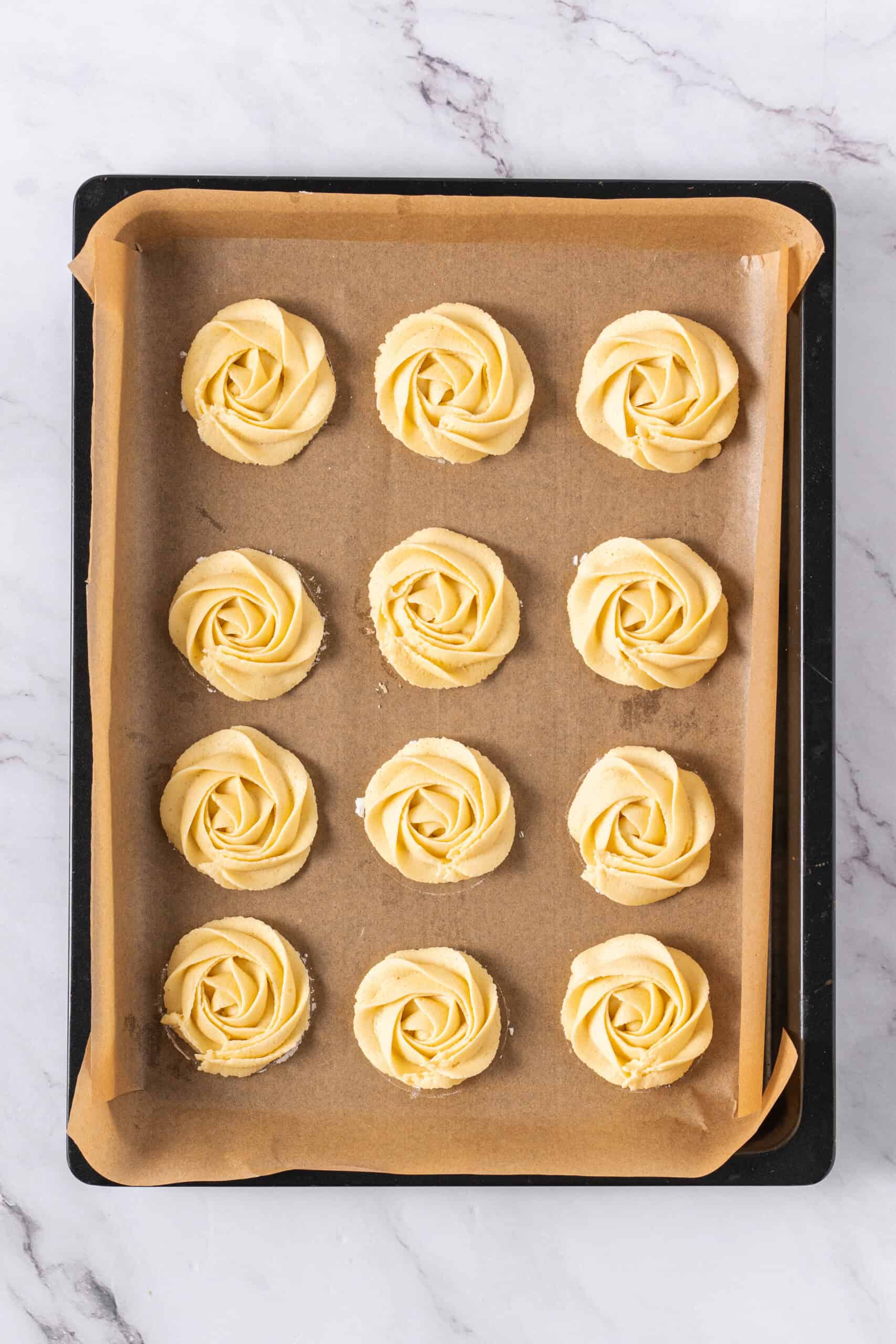 Piped butter cookies arranged on a parchment-lined baking sheet.