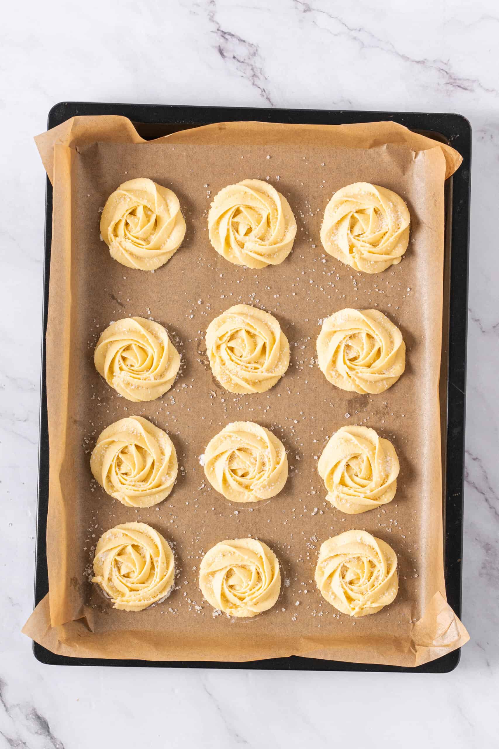 Piped butter cookies topped with coarse sugar on a parchment-lined baking sheet.