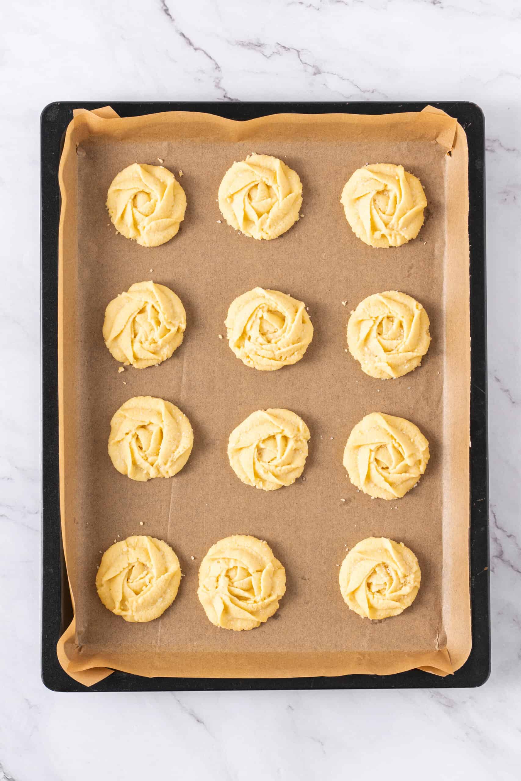 Baked butter cookies cooling on a parchment-lined baking sheet.