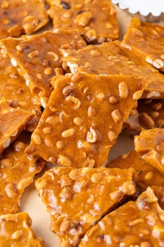 Close-up of golden homemade peanut brittle pieces with glossy caramel and roasted peanuts.