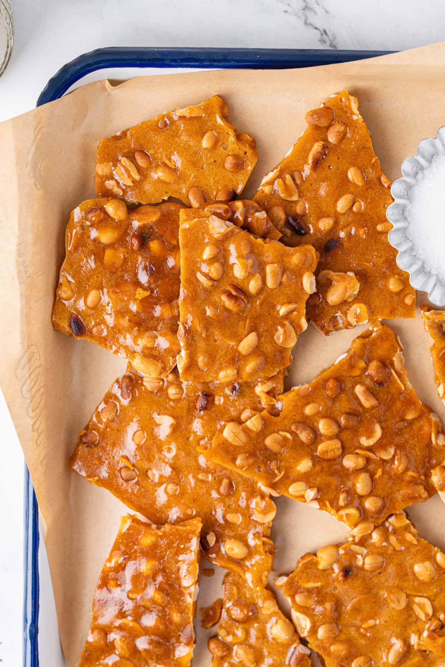 Close-up of golden homemade peanut brittle broken into pieces on a parchment-lined tray.