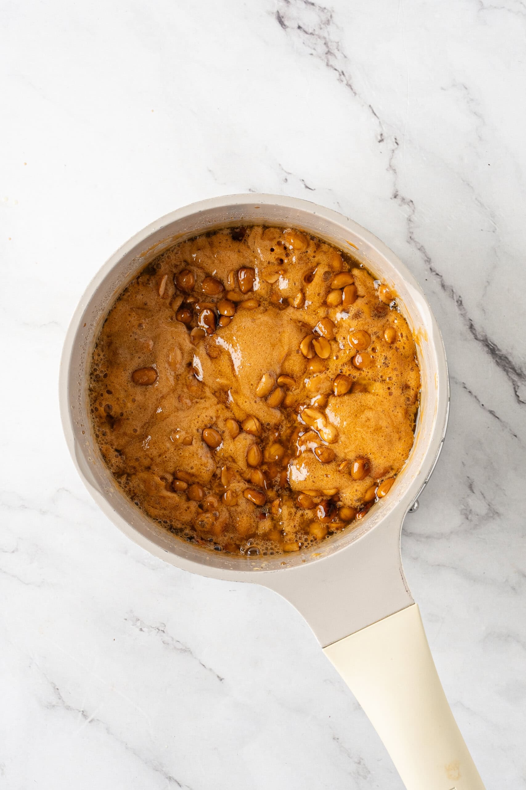 Foamy caramel mixture with peanuts in a saucepan after adding baking soda.