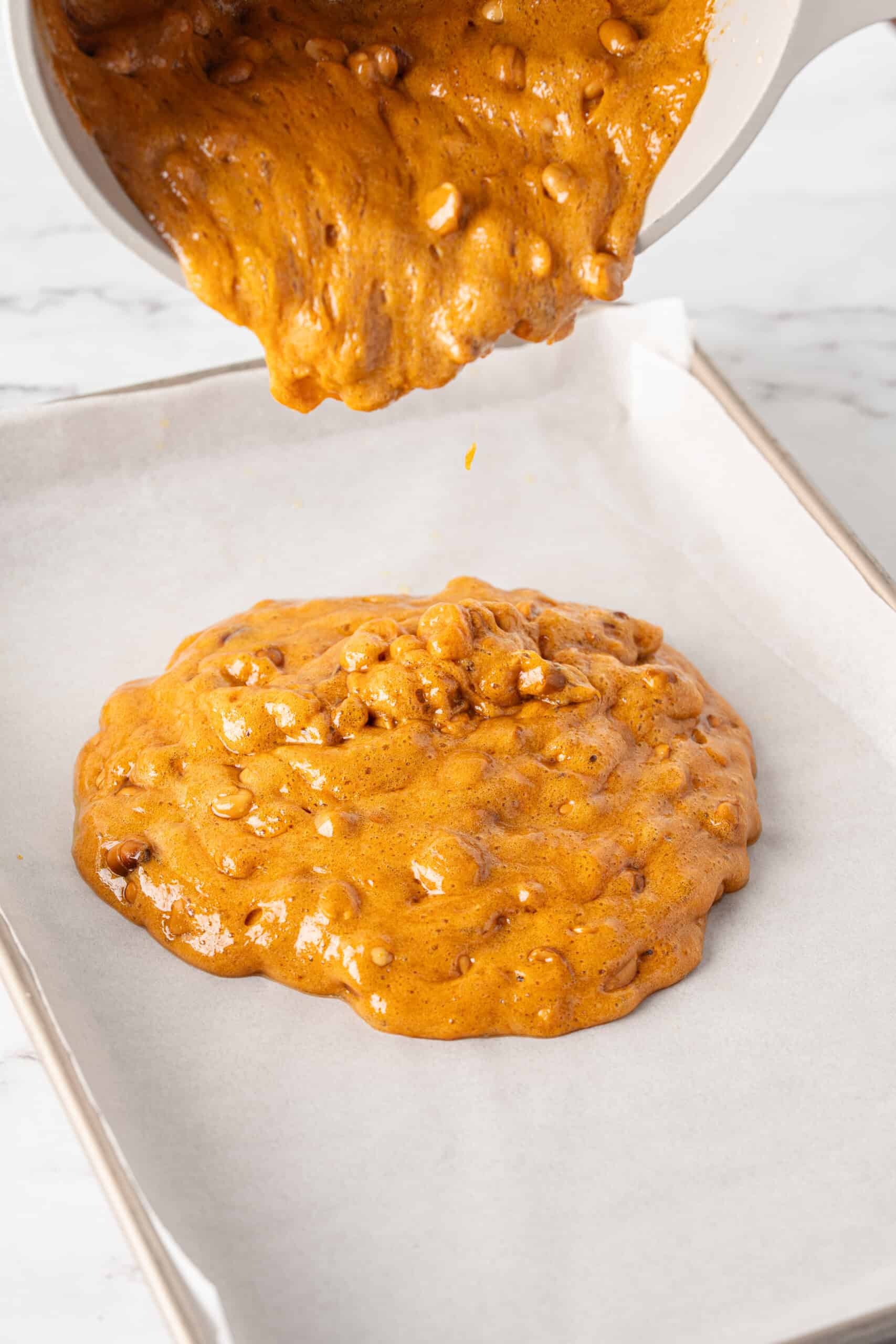 Hot caramel and peanut mixture being poured onto a parchment-lined baking sheet.