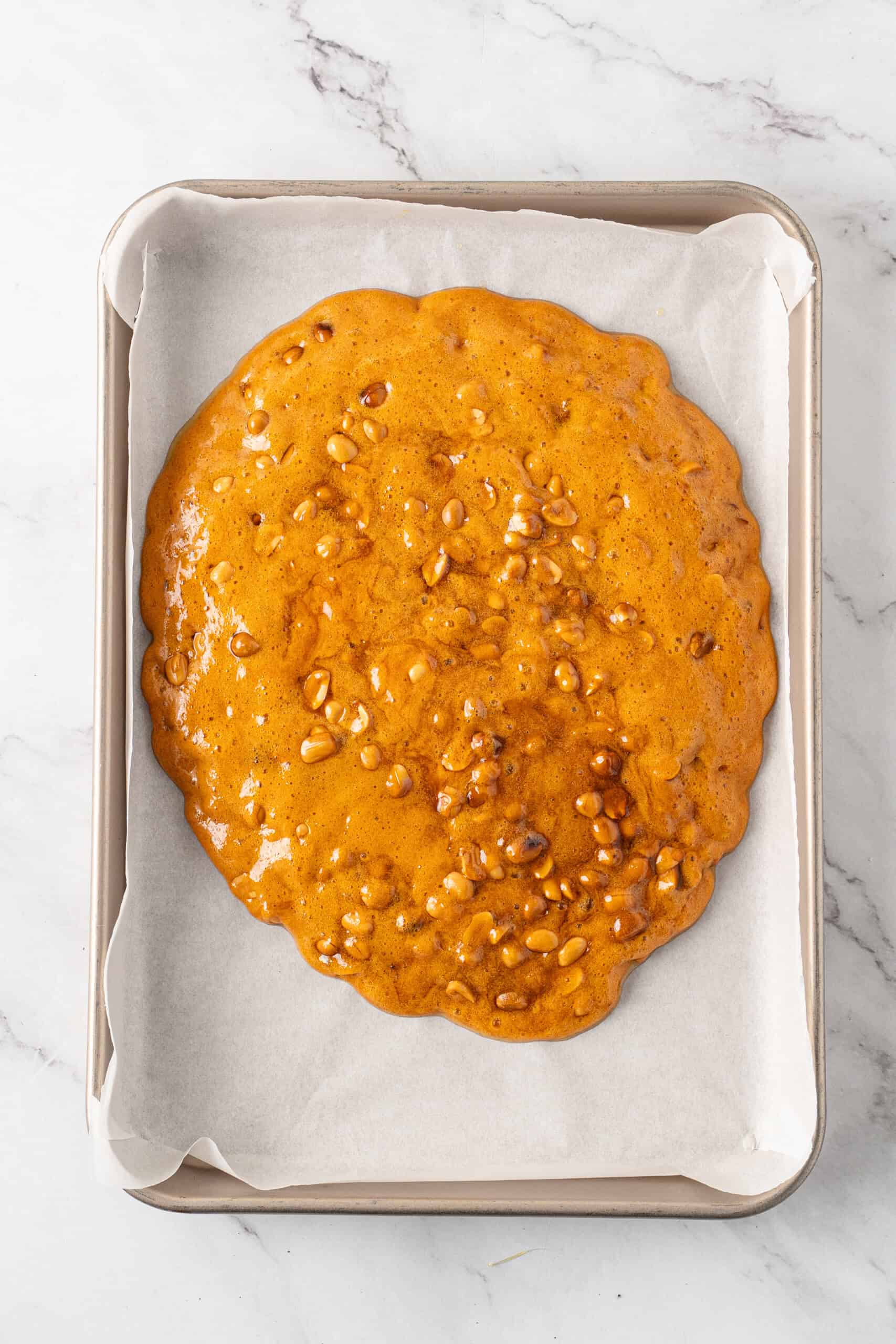 Golden peanut and caramel mixture spread onto a parchment-lined baking sheet to cool and harden.