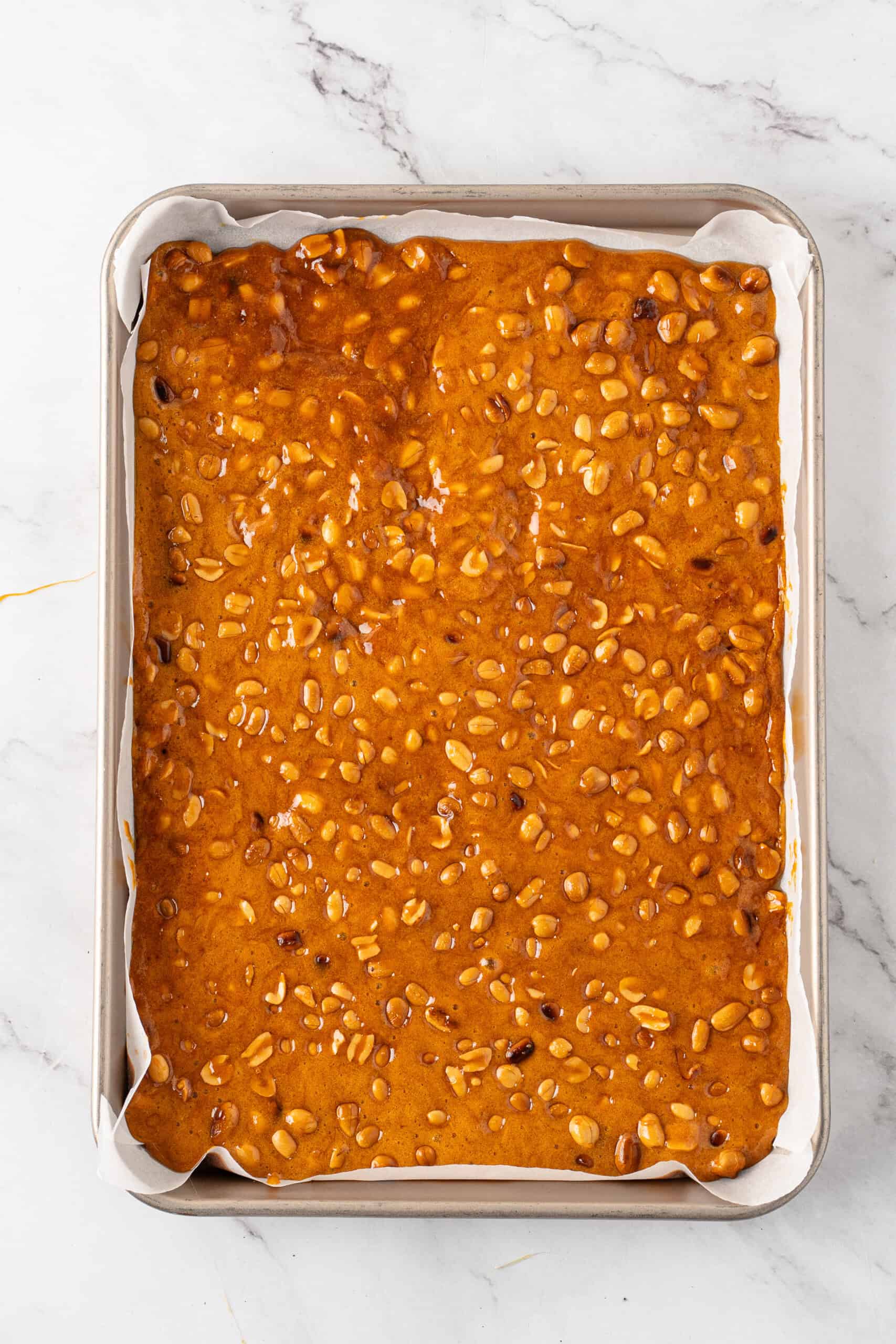 Thin layer of golden caramel and peanuts spread evenly across a parchment-lined baking sheet.