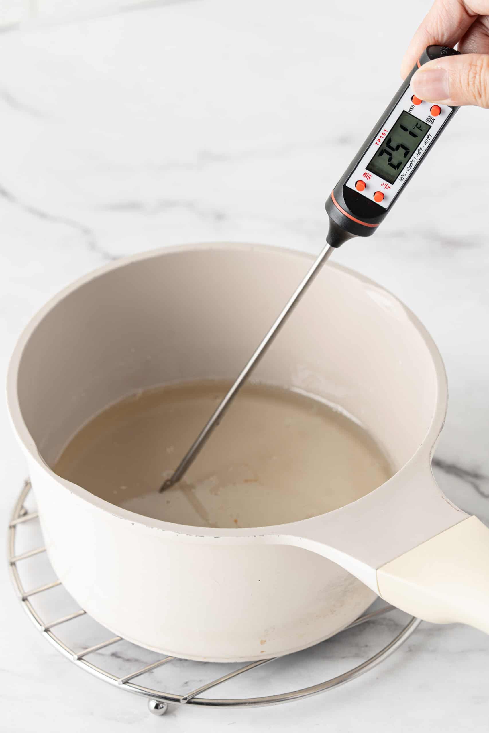 Checking the temperature of the sugar syrup in a saucepan with a digital candy thermometer.