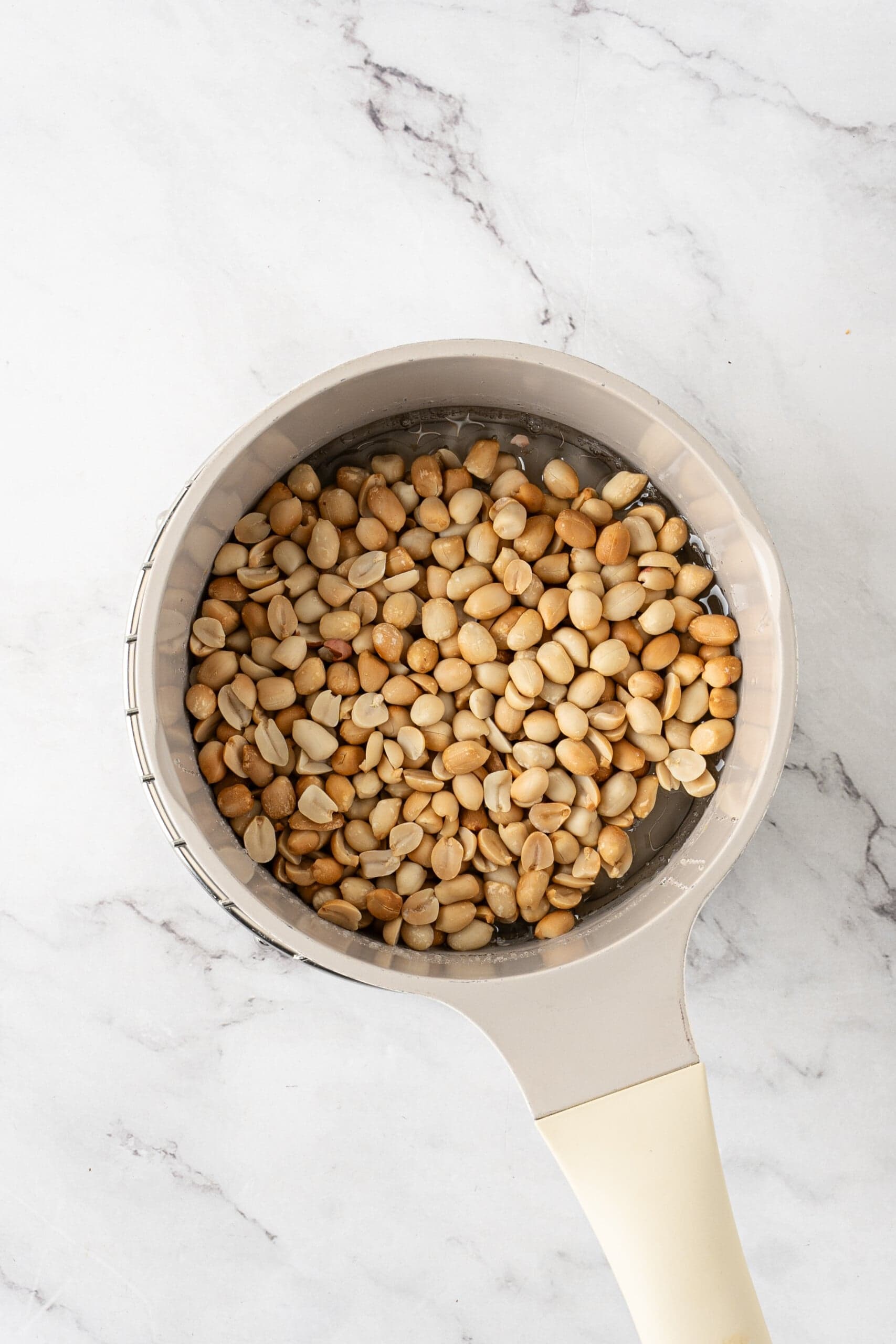 Peanuts added to a saucepan of sugar syrup.