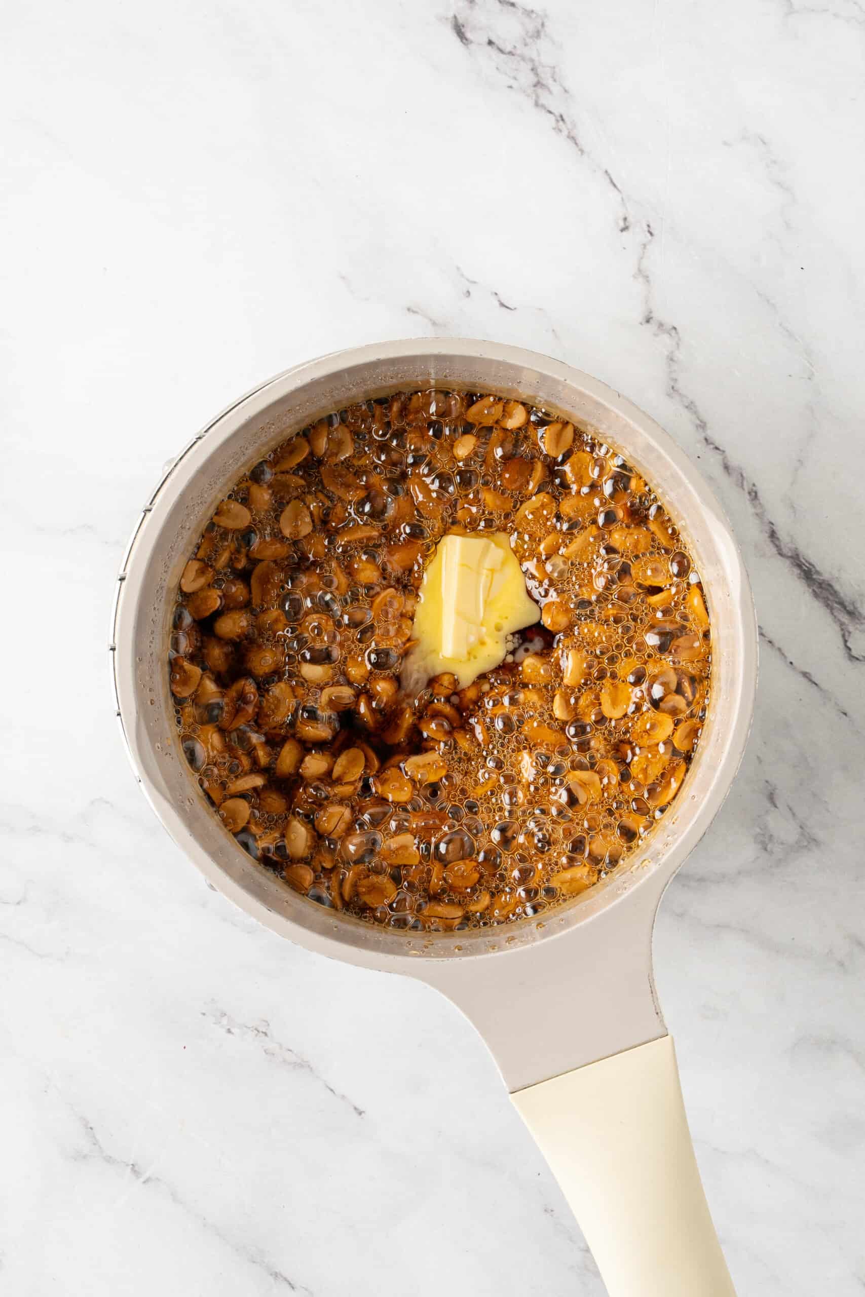 Butter added to a saucepan of bubbling caramel syrup and peanuts.
