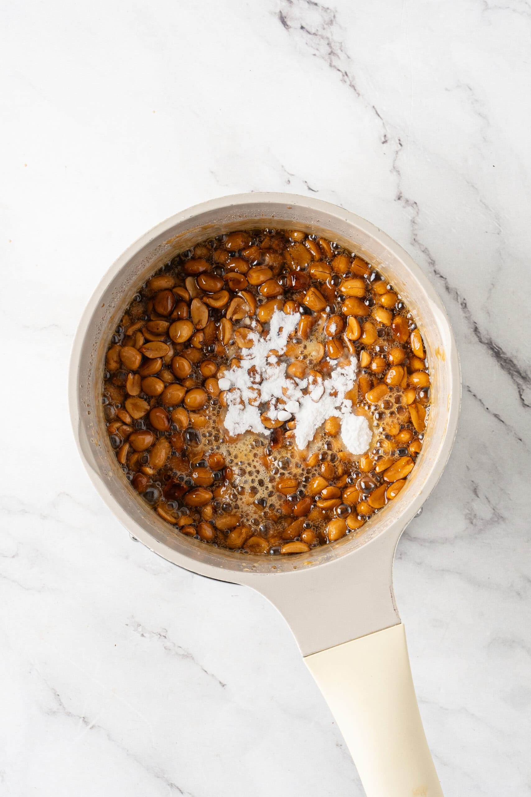 Baking soda added to a saucepan of bubbling caramel and peanuts.