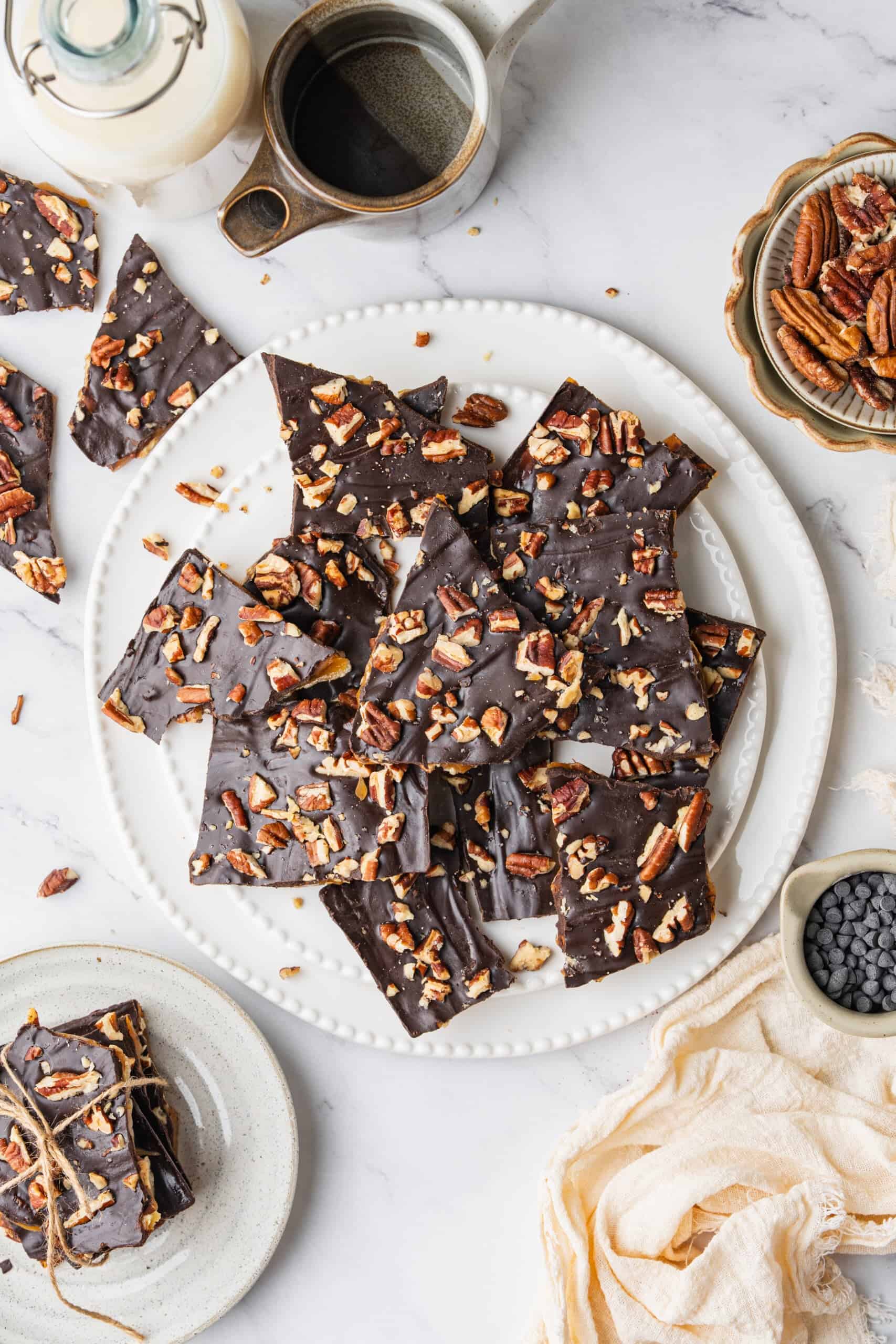 Homemade Toffee with buttery caramel, rich chocolate, and chopped pecans arranged on a white platter with extra pieces on the side.
