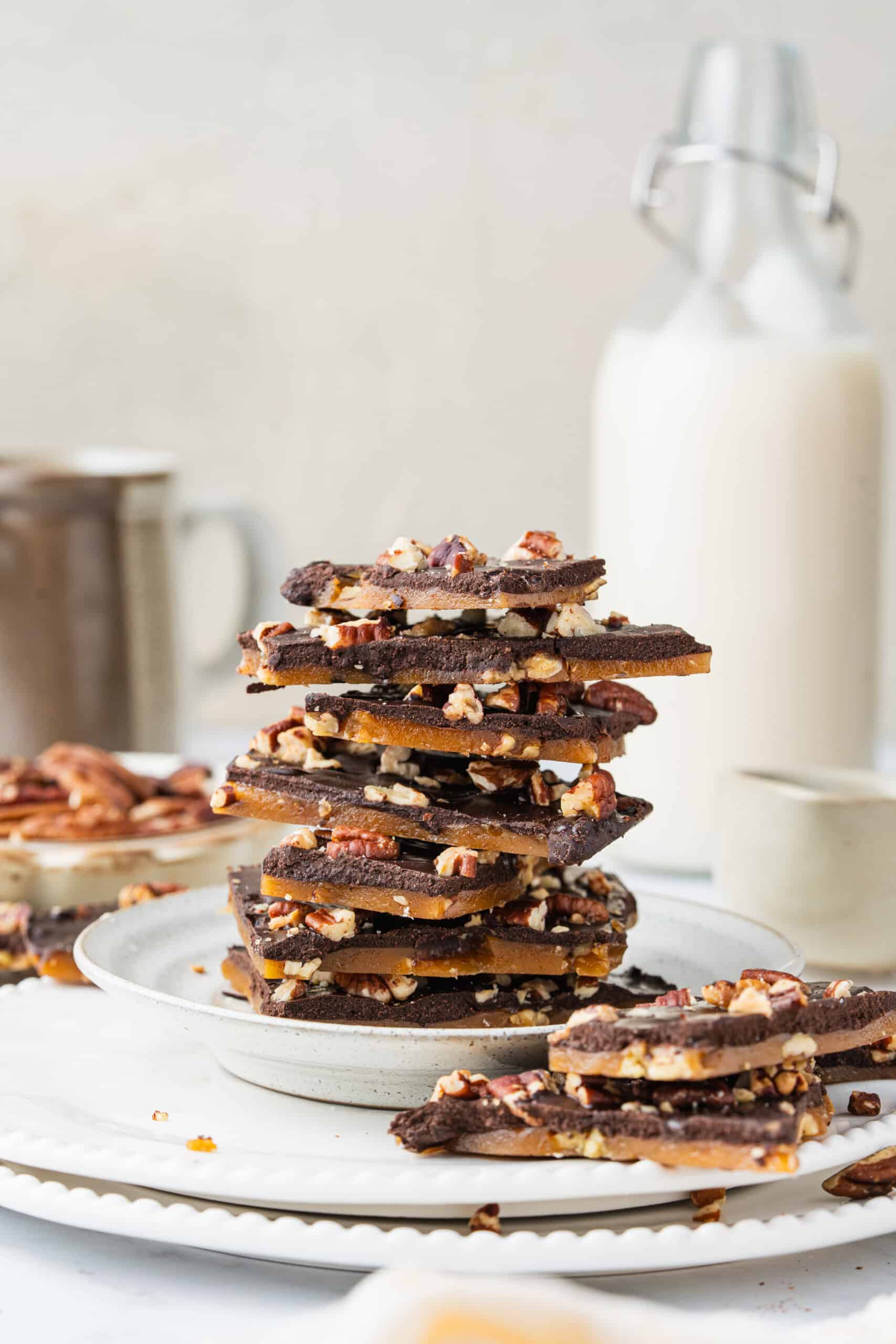 Homemade Toffee stacked on a ceramic plate, showing layers of golden buttery toffee, dark chocolate, and chopped pecans.