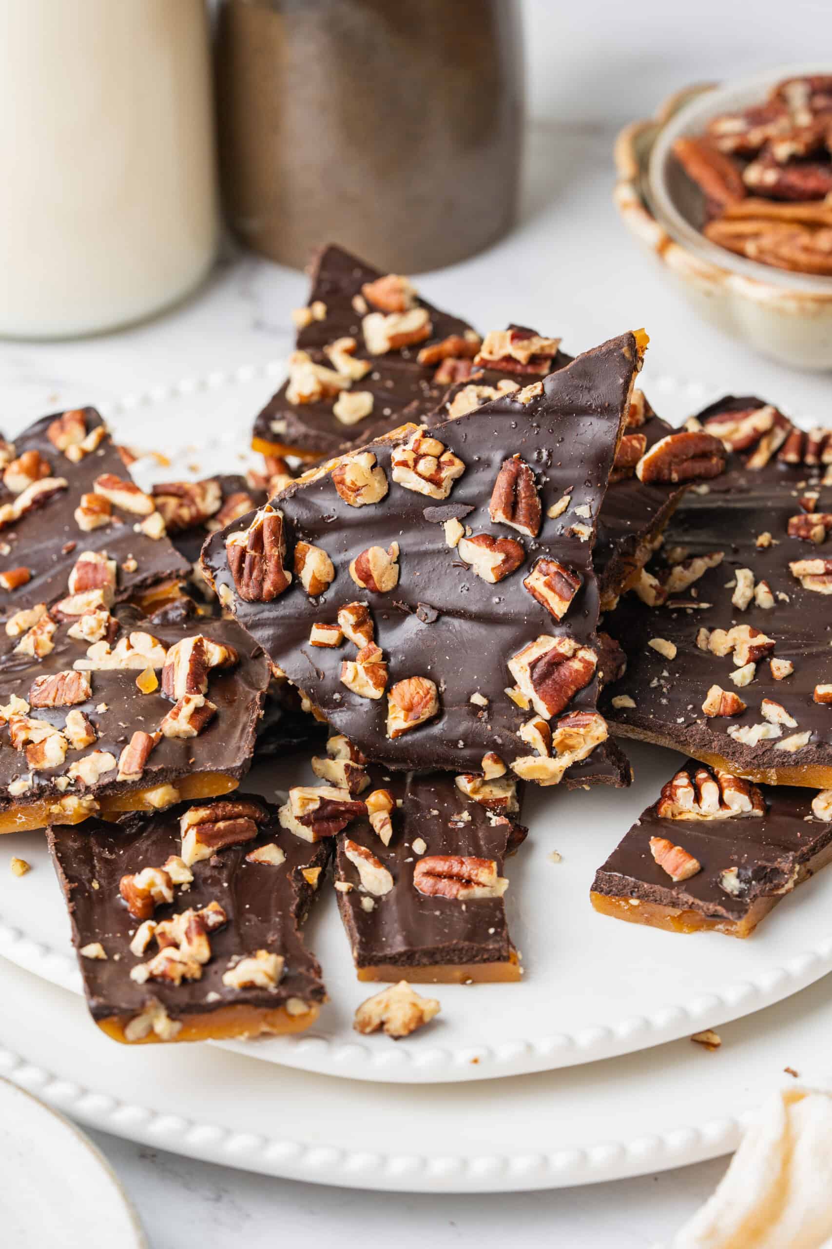 Homemade Toffee with buttery caramel layers, rich chocolate, and chopped pecans stacked on a white plate.