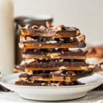 Homemade Toffee stacked on a ceramic plate, showing layers of golden buttery toffee, dark chocolate, and chopped pecans.