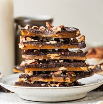 Homemade Toffee stacked on a ceramic plate, showing layers of golden buttery toffee, dark chocolate, and chopped pecans.
