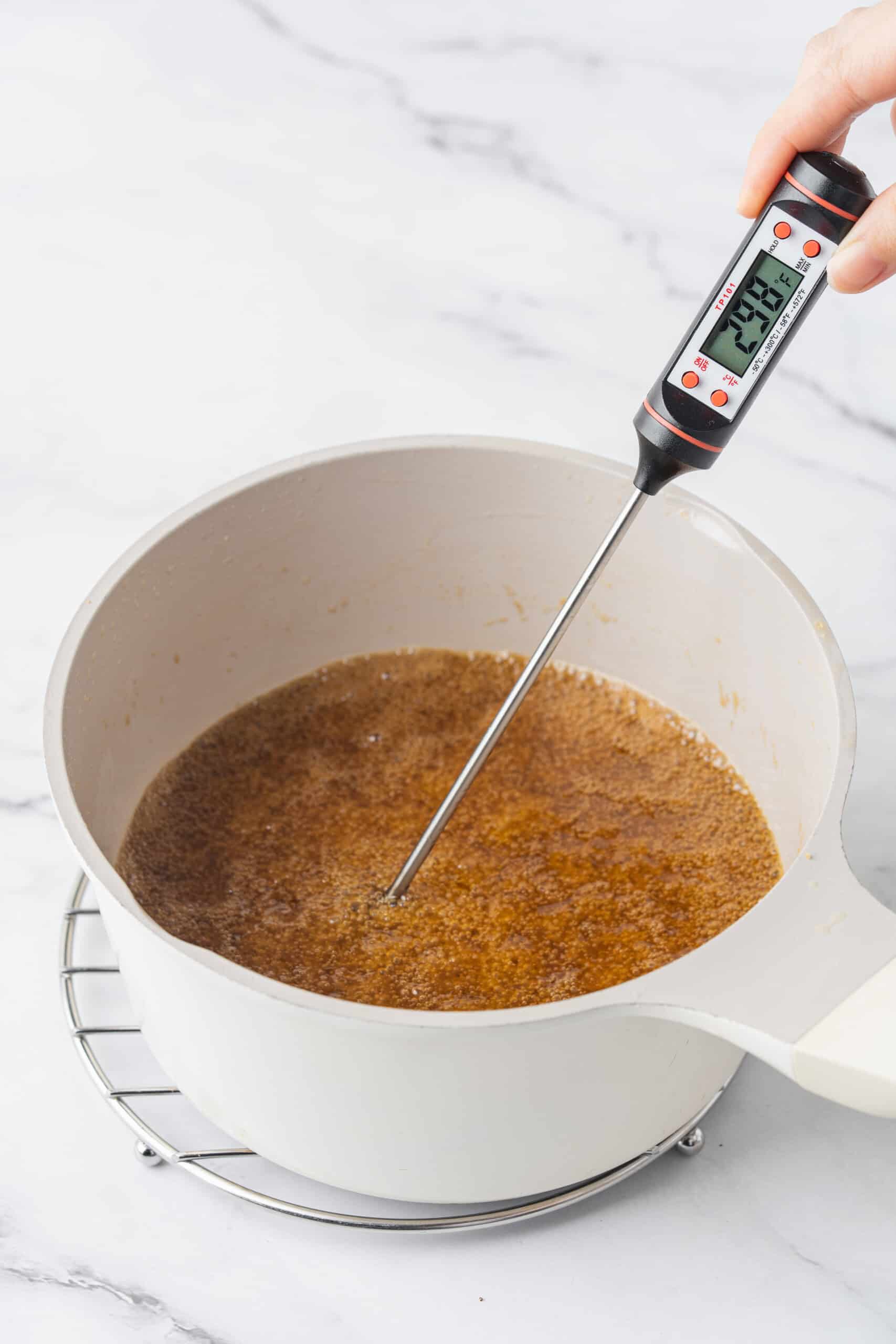 A digital thermometer measuring the temperature of a bubbling golden-brown butter and sugar mixture in a saucepan.